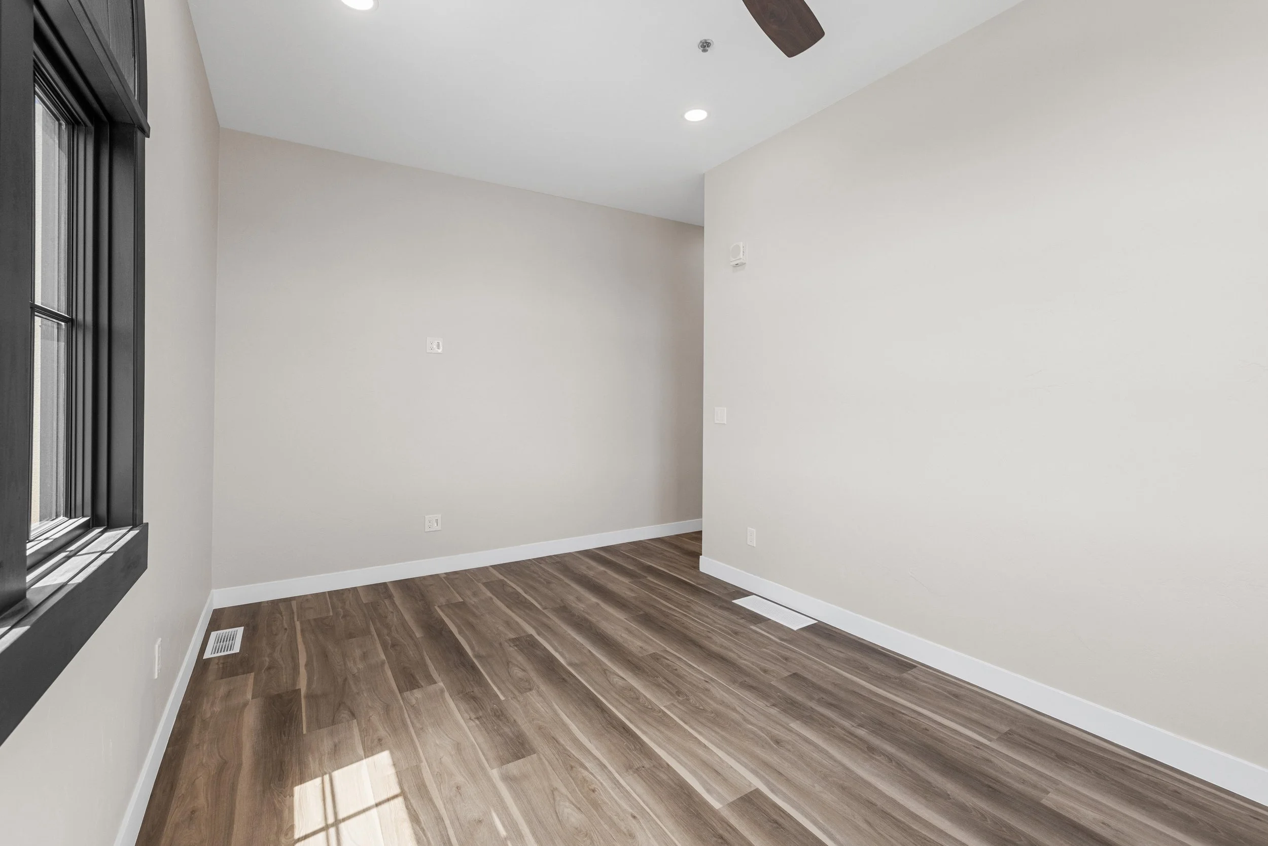 Empty room with wood flooring, light-colored walls, a window with black trim, and ceiling light