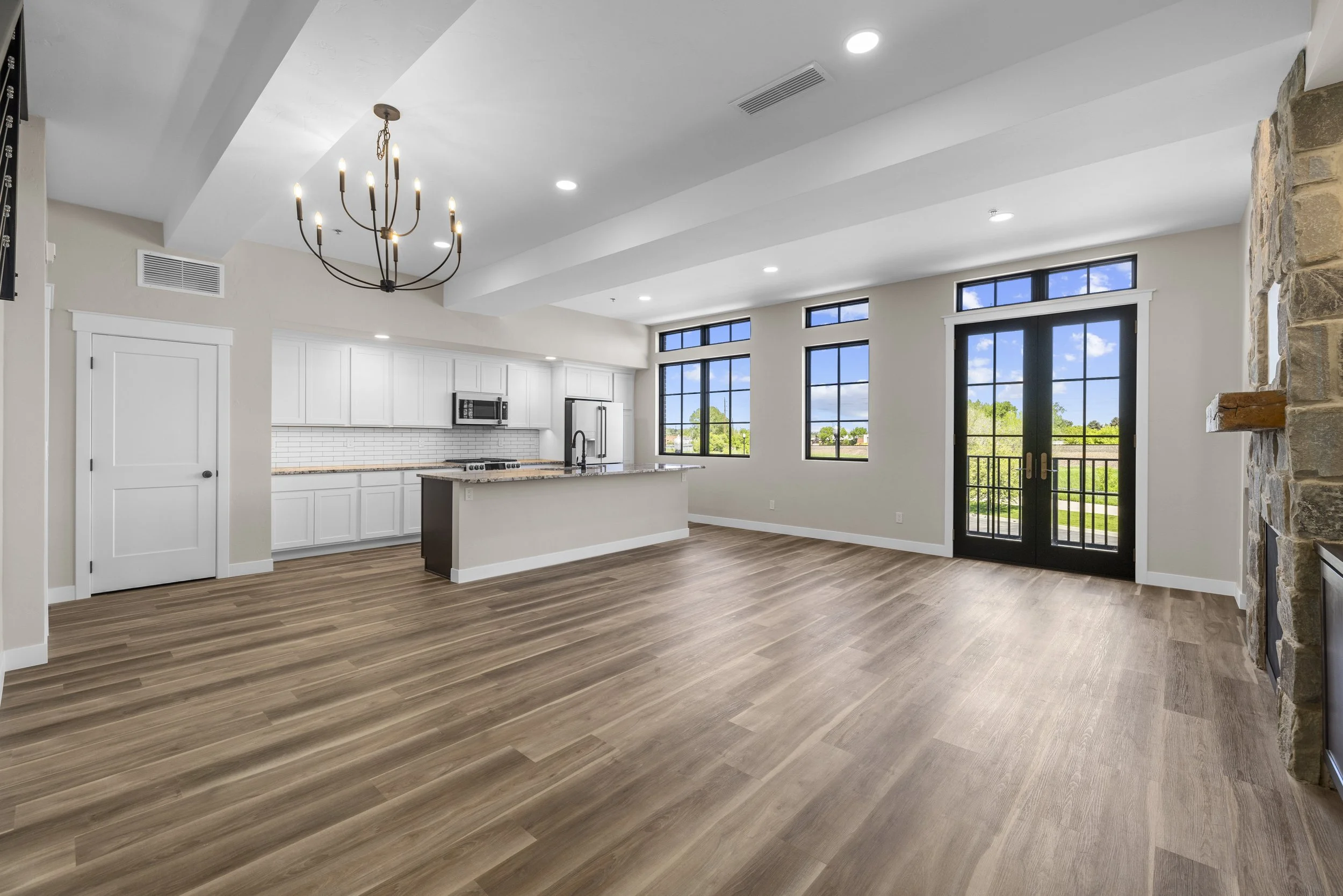 Open-concept living room and kitchen inside an Ice Haus Condo for sale in Sheridan, Wyoming, featuring hardwood floors,a  stone fireplace, large windows, and modern finishes.