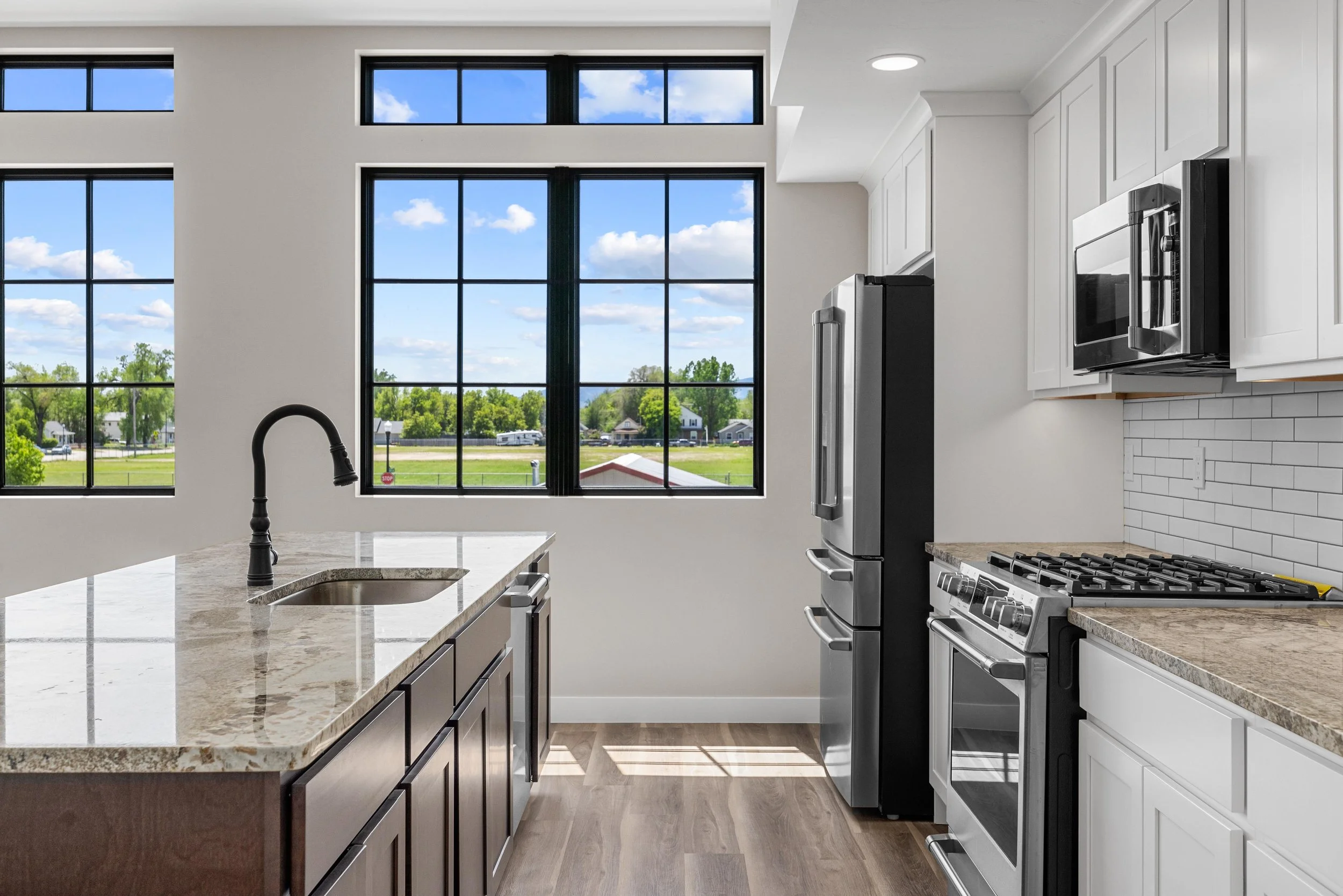 Modern kitchen in an Ice Haus Condo for sale in Sheridan, Wyoming, with large windows, white cabinets, stainless steel appliances, granite countertops, and a black faucet.