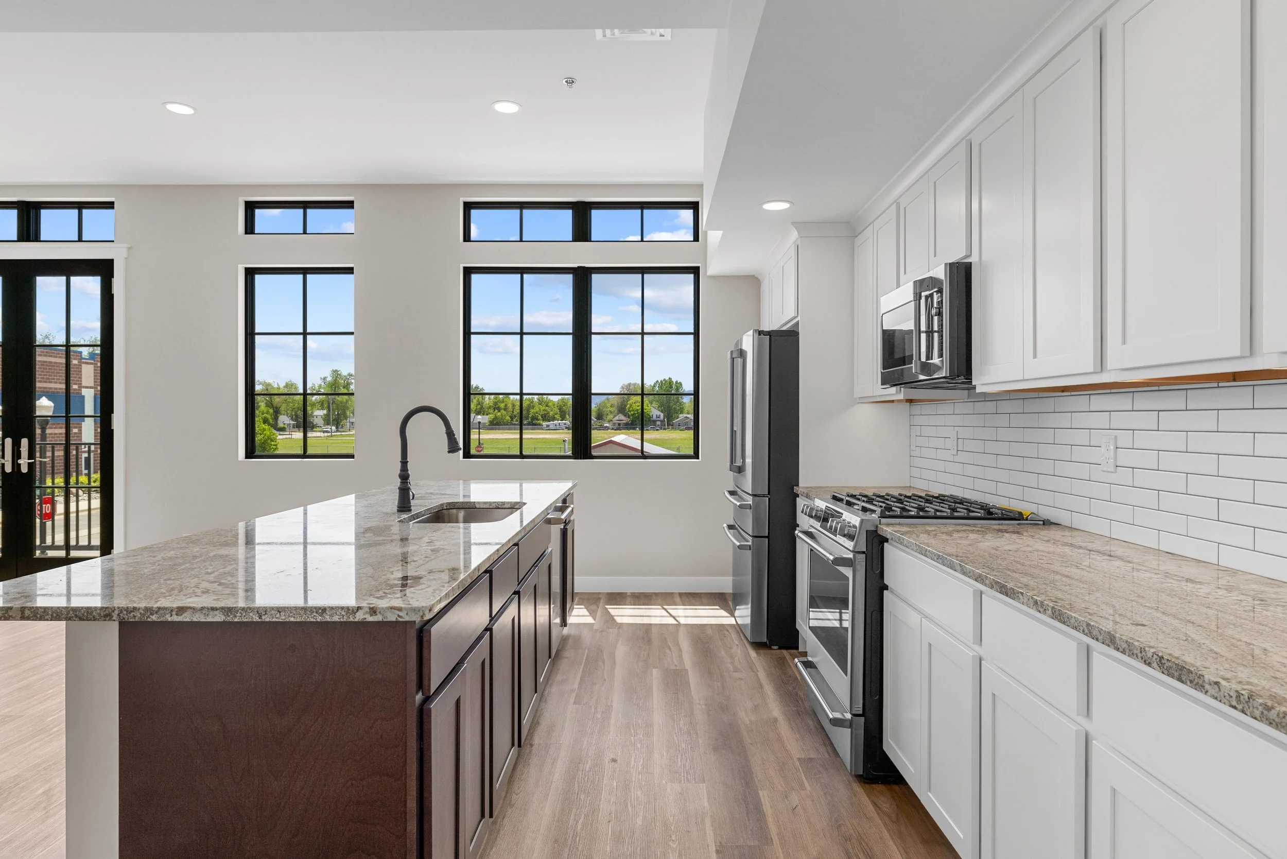 Modern kitchen in an Ice Haus Condo for sale in Sheridan, Wyoming, with white cabinets, granite countertops, stainless steel appliances, large windows, and hardwood floors.