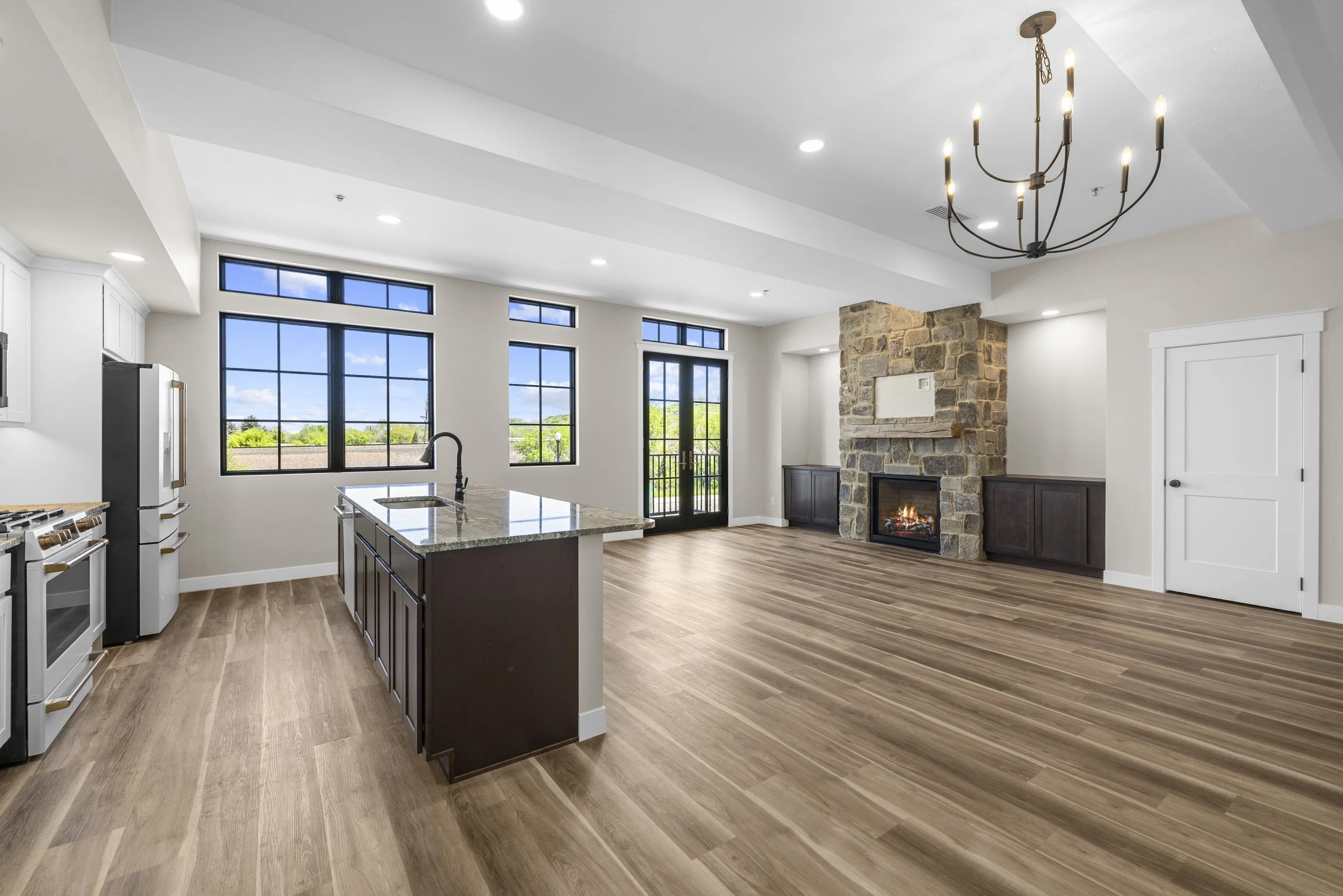 Spacious open-plan kitchen and living area with large windows, a stone fireplace, and a wooden floor.