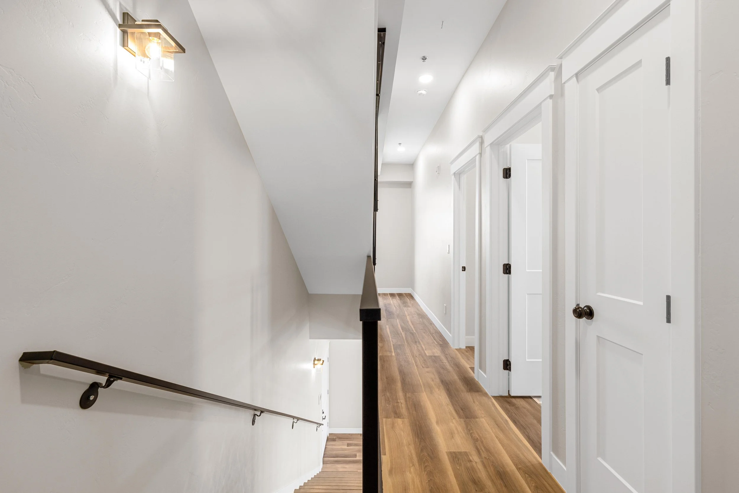Split view of a staircase and a hallway in a modern home, with white walls, wooden floors, and white doors.