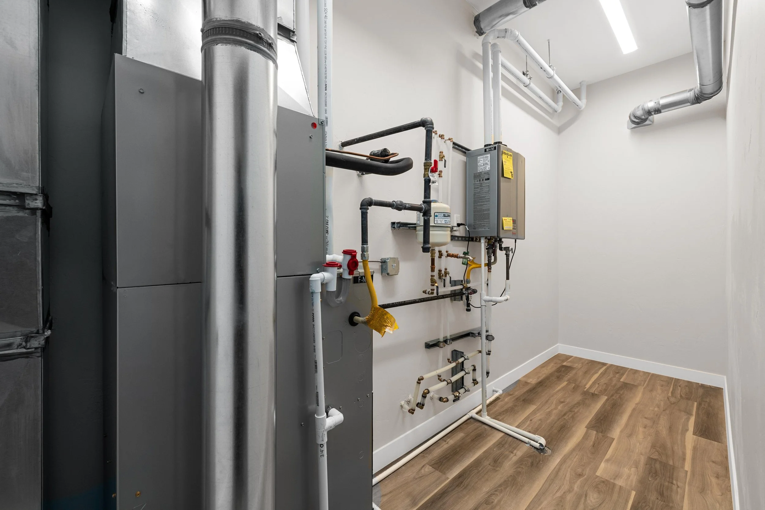 An empty utility room with heating equipment, pipes, and wood-like flooring.
