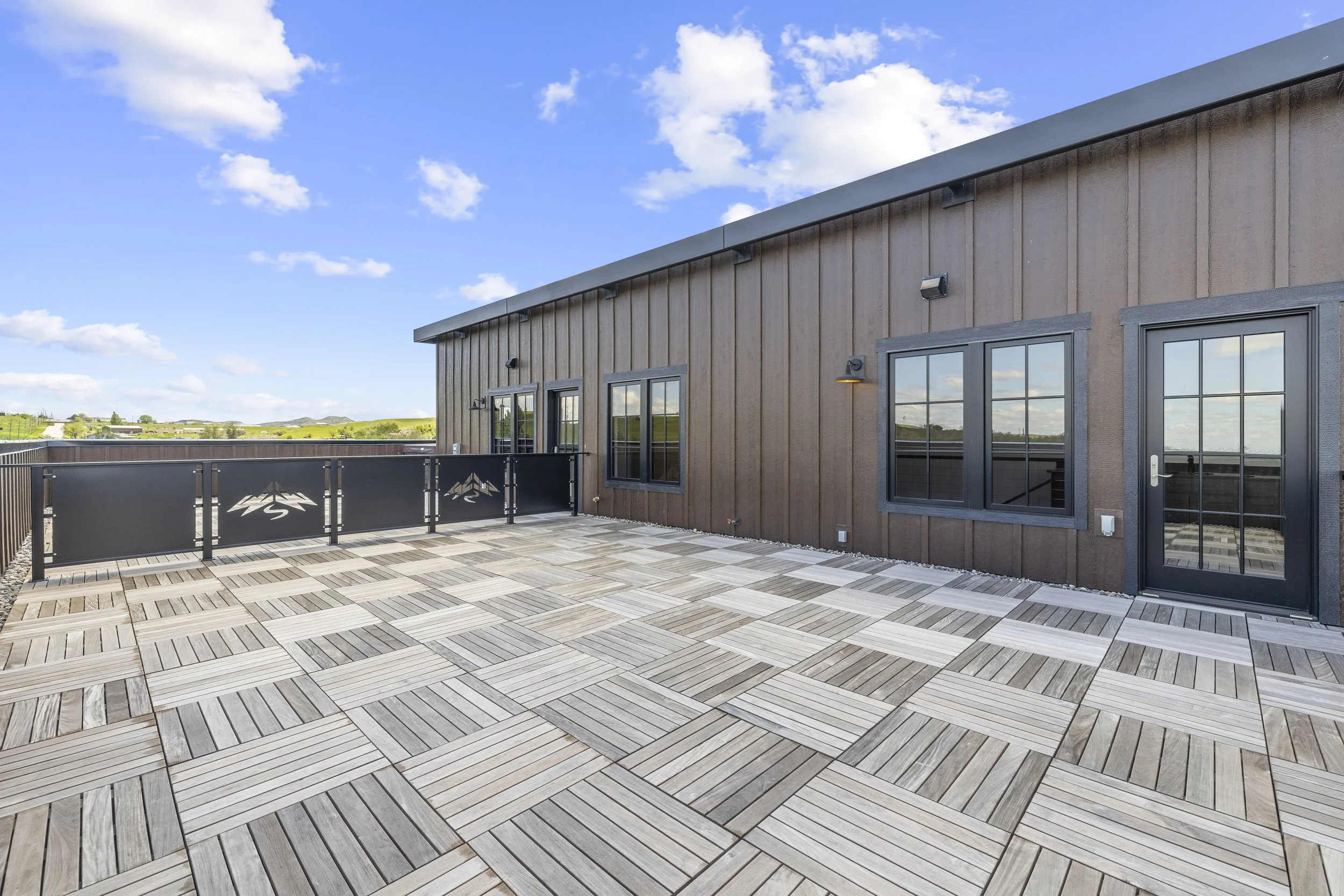 Shared rooftop terrace at Ice Haus Condos for sale in Sheridan, WY featuring wood tile flooring, modern railing, outdoor lighting, and expansive sky views.