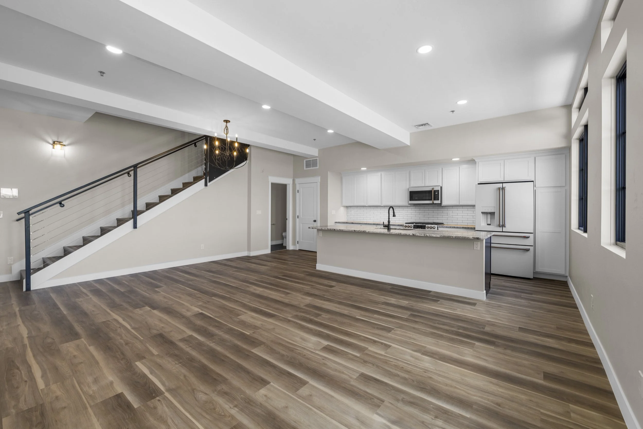 Open plan living area with kitchen, white cabinets, gray island, hardwood floors, and stairs leading to upper level.