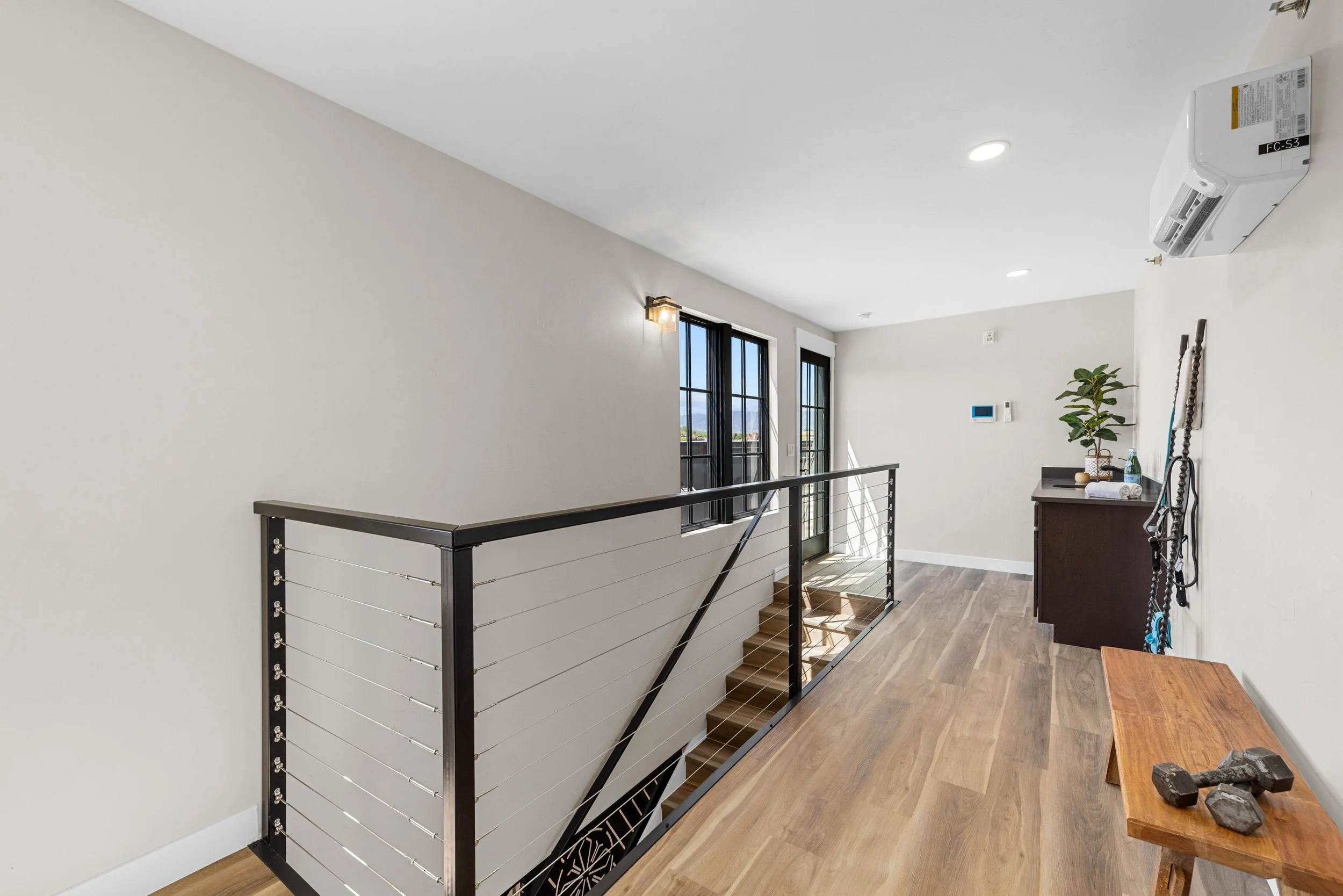 Interior in an Ice Haus Condo for sale in Sheridan, Wyoming, with wood flooring, black railing by stairs, a small table with rocks, a dark wood cabinet, potted plant, and a wall-mounted control panel.