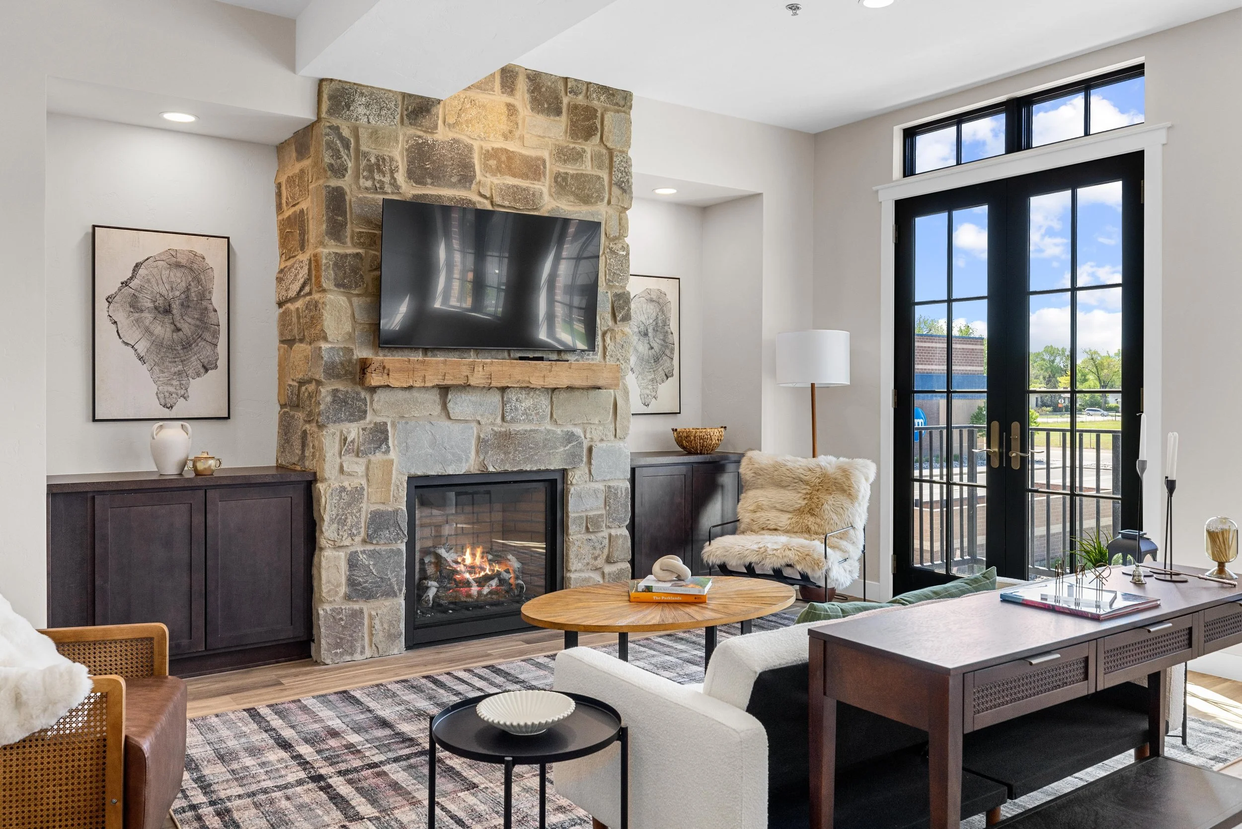 Modern living room inside an Ice Haus Condo in Sheridan, WY with stone fireplace, mounted TV, sliding glass door, dark wood cabinetry, and open-concept design.