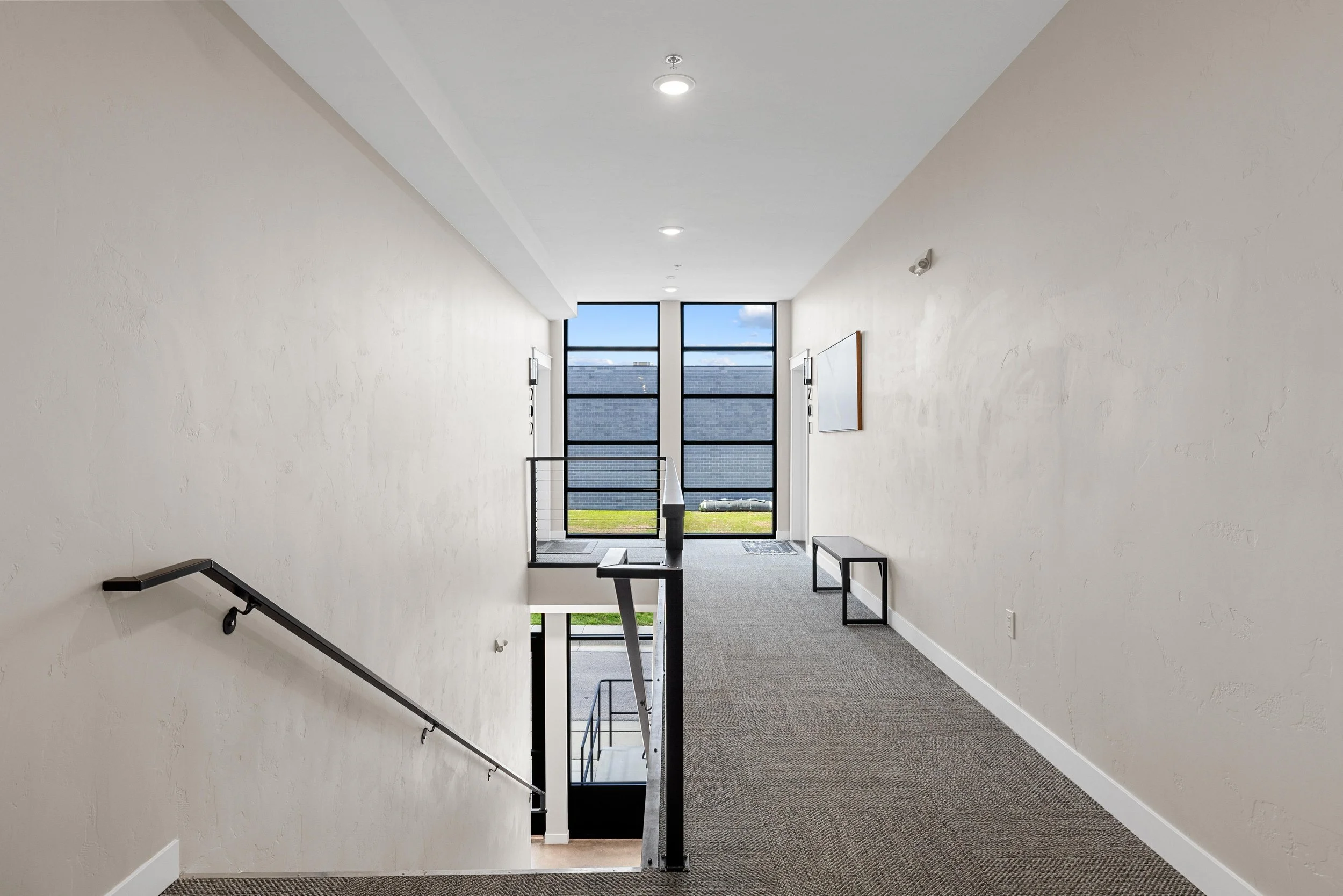 Interior corridor with staircase, large windows at the end, and minimal decor.