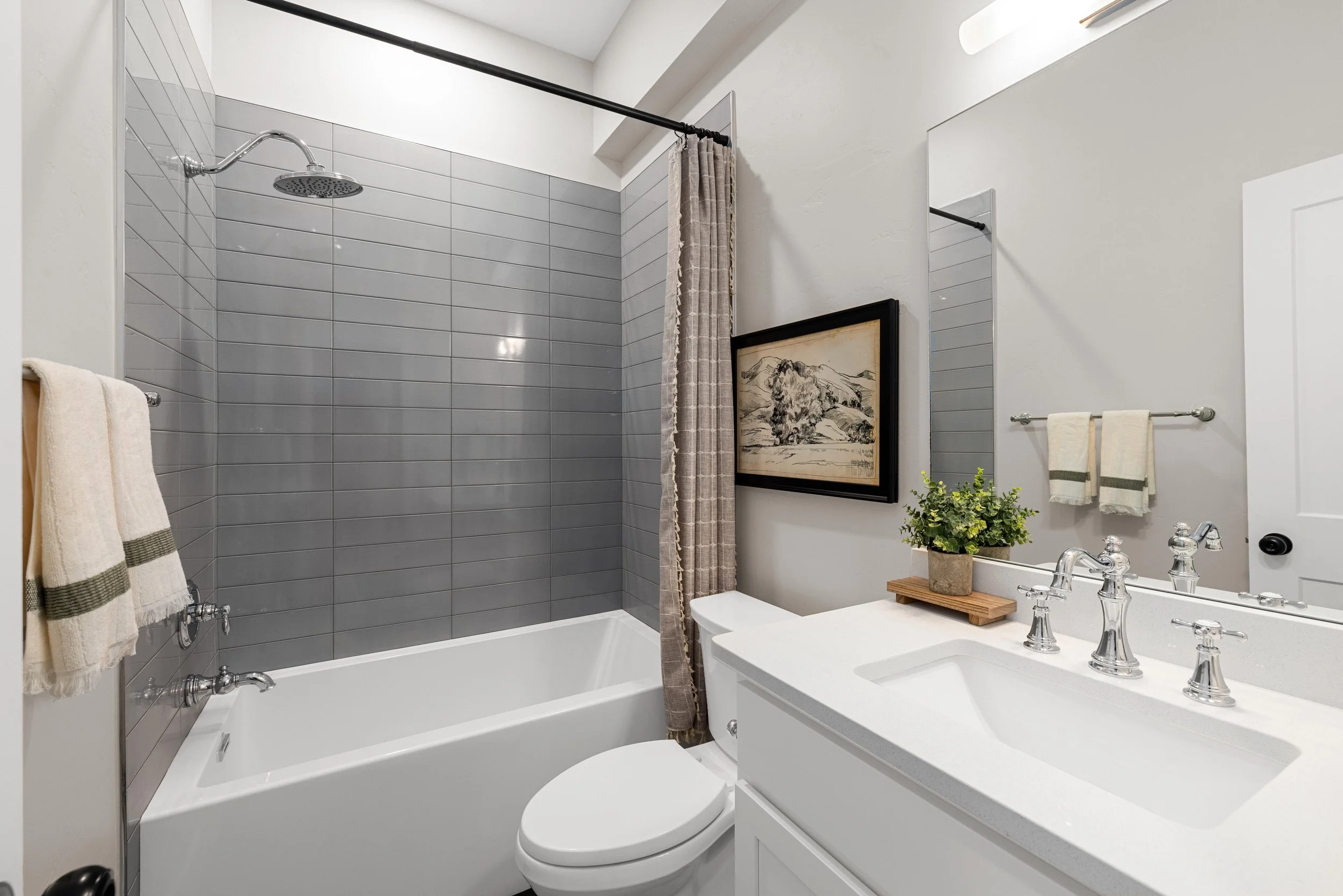 Modern bathroom inside an Ice Haus Condo in Sheridan, Wyoming that is for sale featuring a bathtub and shower with gray tile, white vanity, and contemporary finishes.