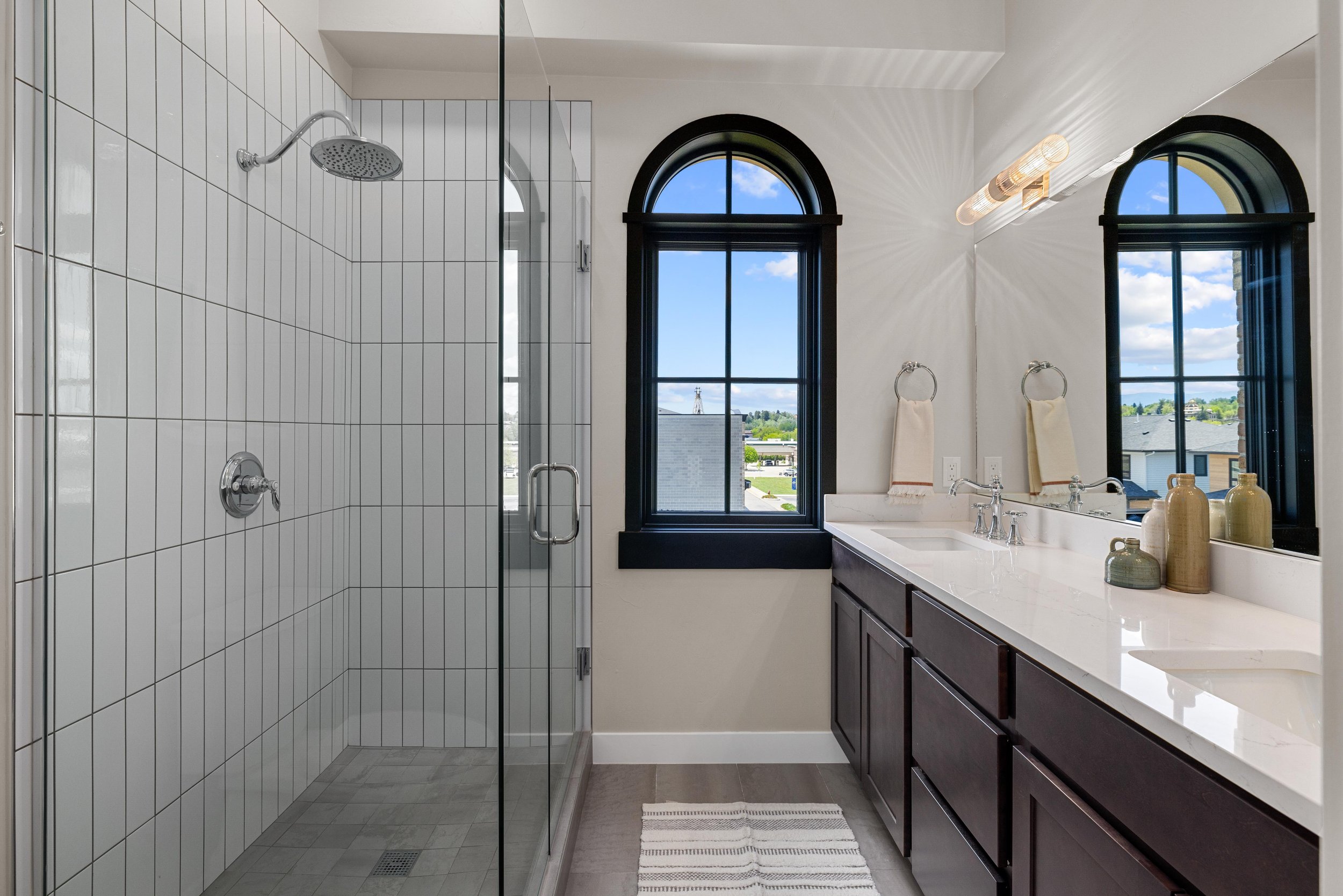 Luxury bathroom inside an Ice Haus Condo for sale in Sheridan, WY with glass-enclosed shower, arched windows, dark wood vanity, and modern design.