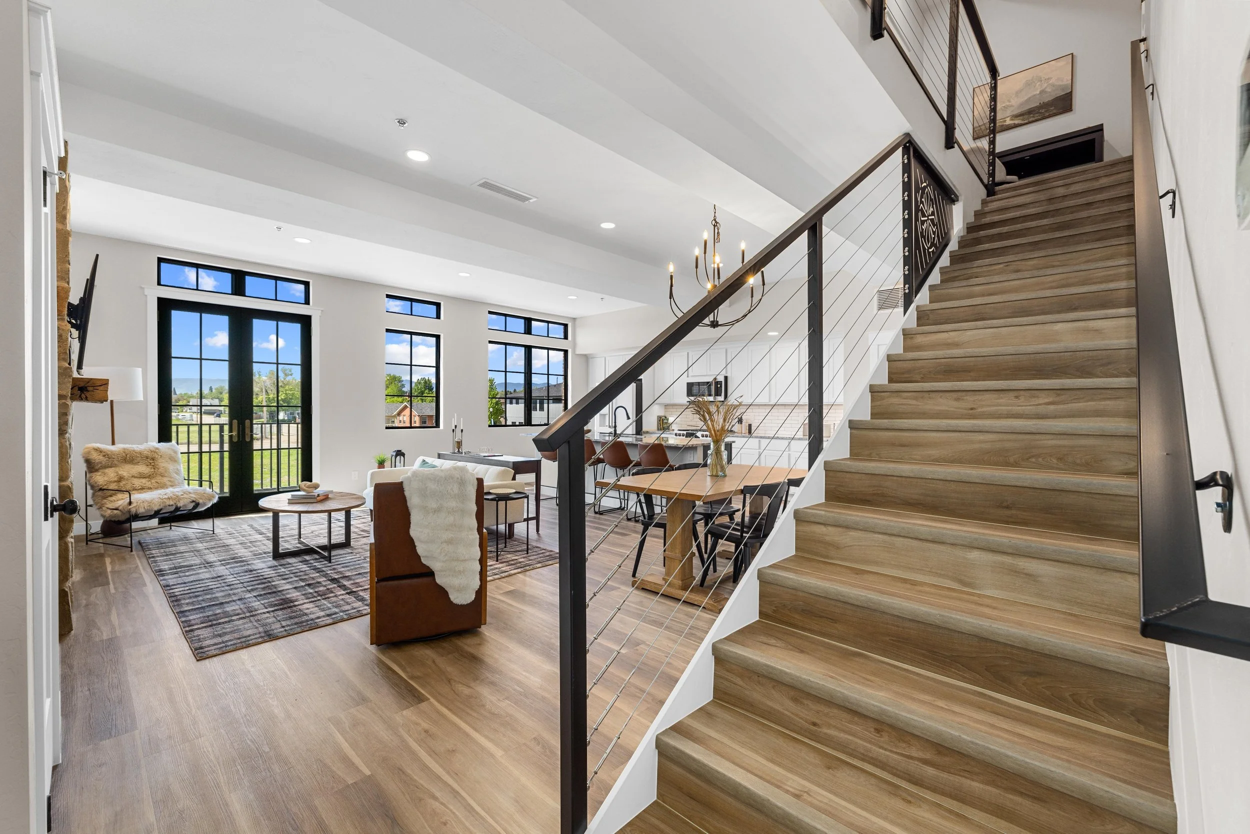 Open-concept living room inside an Ice Haus Condo for sale in Sheridan, WY with hardwood floors, modern staircase, large windows, and bright natural light.