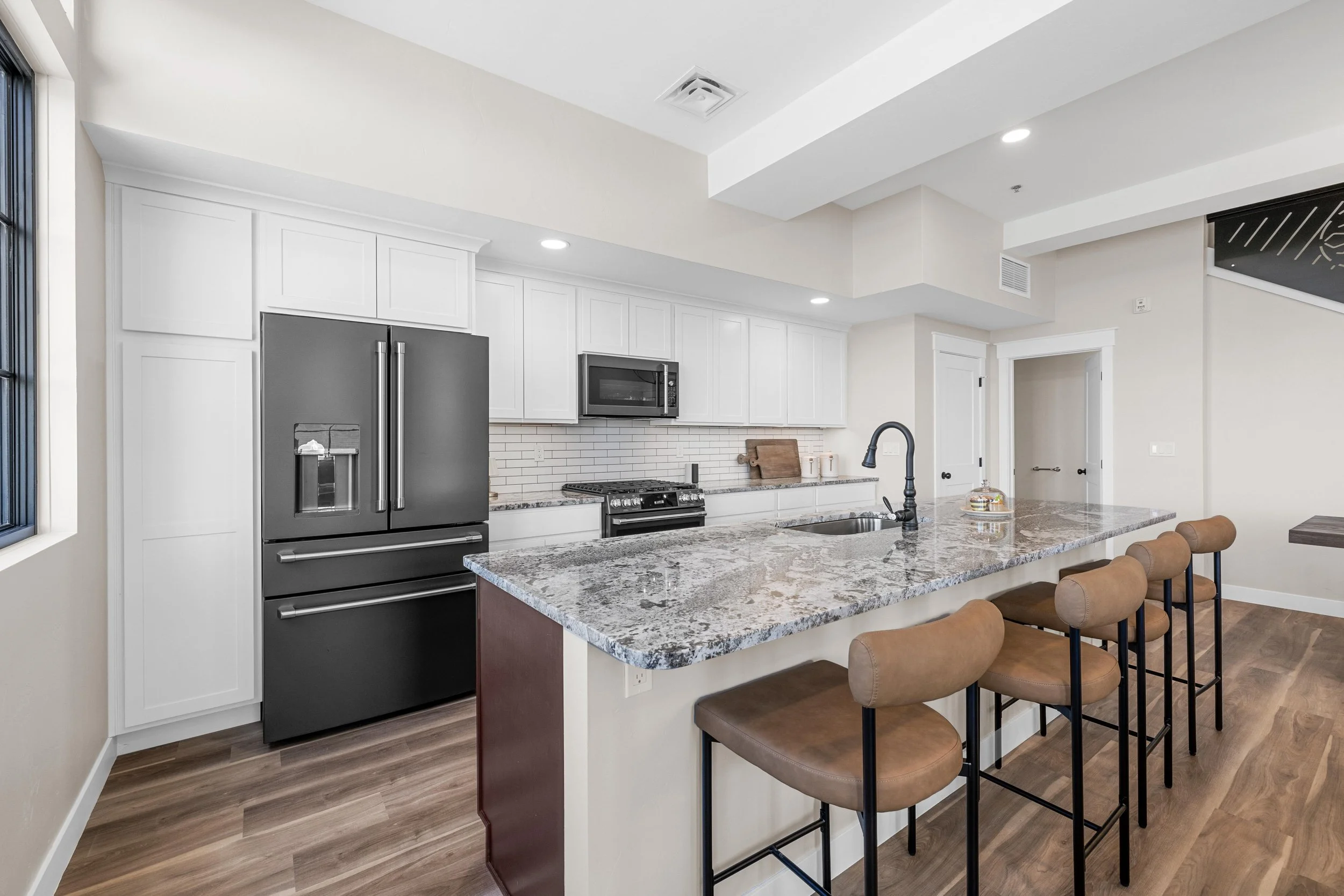 Modern kitchen with white cabinets, black refrigerator, granite countertops, and brown bar stools.