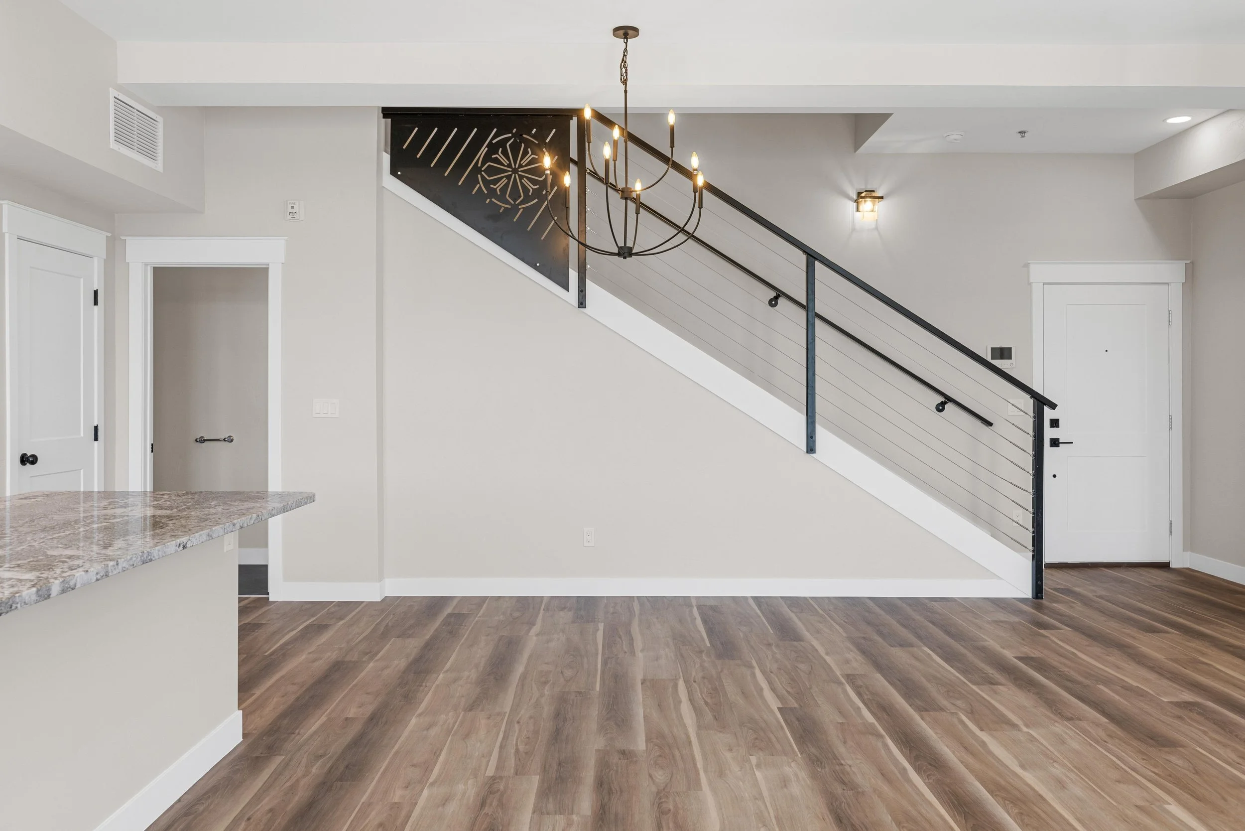 Empty living room with a staircase, chandelier, hardwood floors, and white walls.