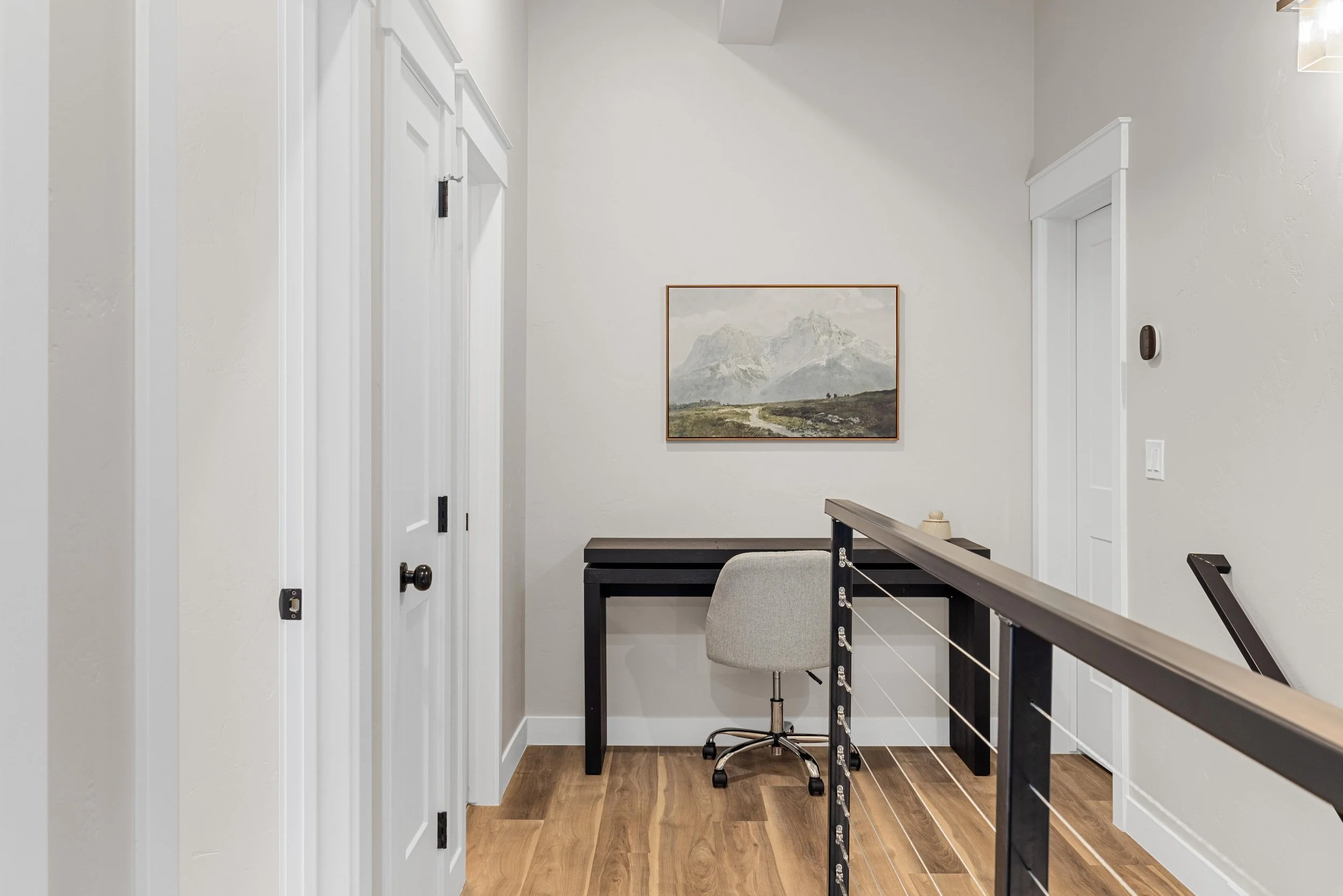 Home office space with a desk, chair, mountain landscape painting, and light-colored walls.