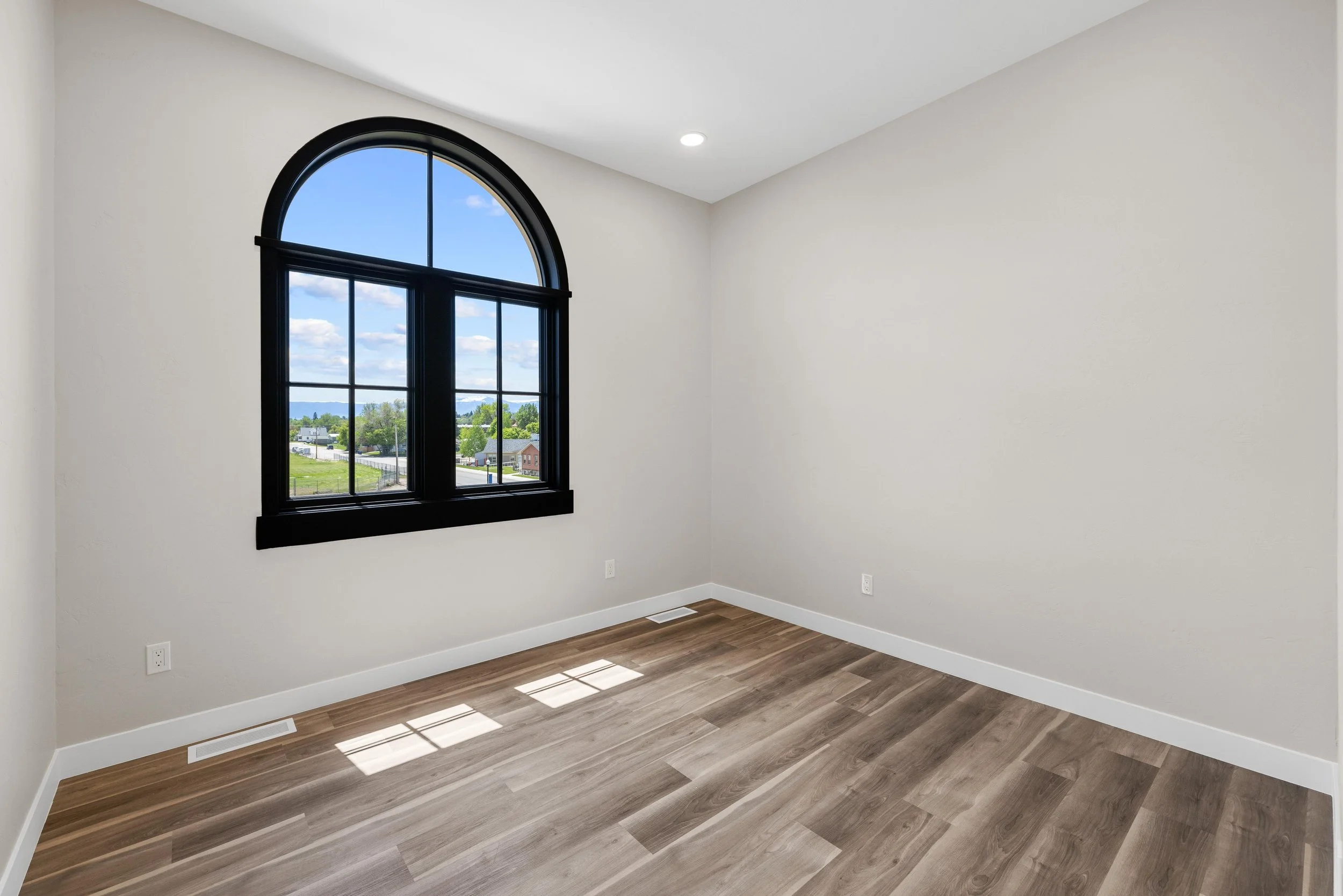 An empty room in an Ice Haus Condo for sale in Sheridan, Wyoming,  with a large arched window, wood flooring, and beige walls.
