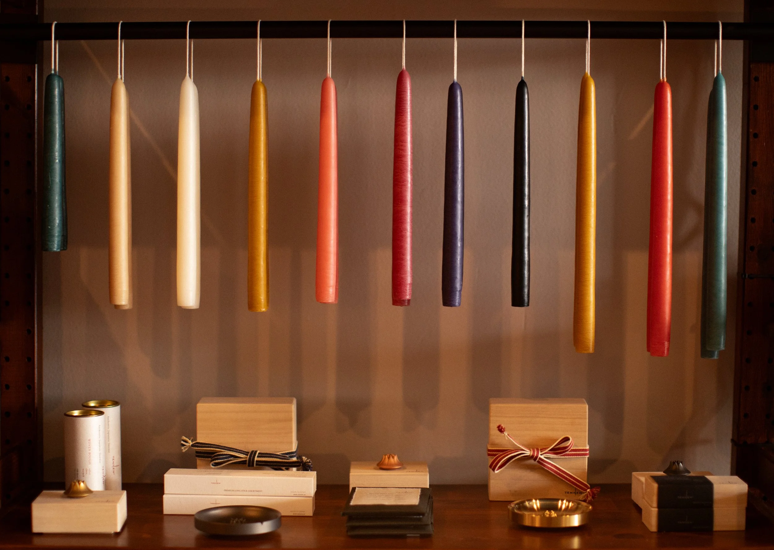 Colorful candles hanging on a rack with various small boxes, jars, and decorative items on a wooden surface below.