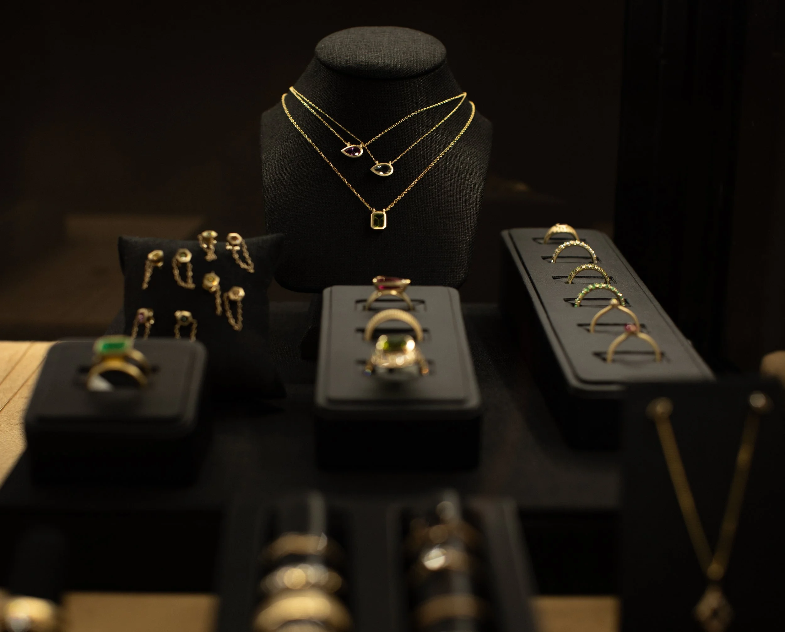 Display of various gold and gemstone jewelry including necklaces, rings, and earrings in a jewelry store showcase.