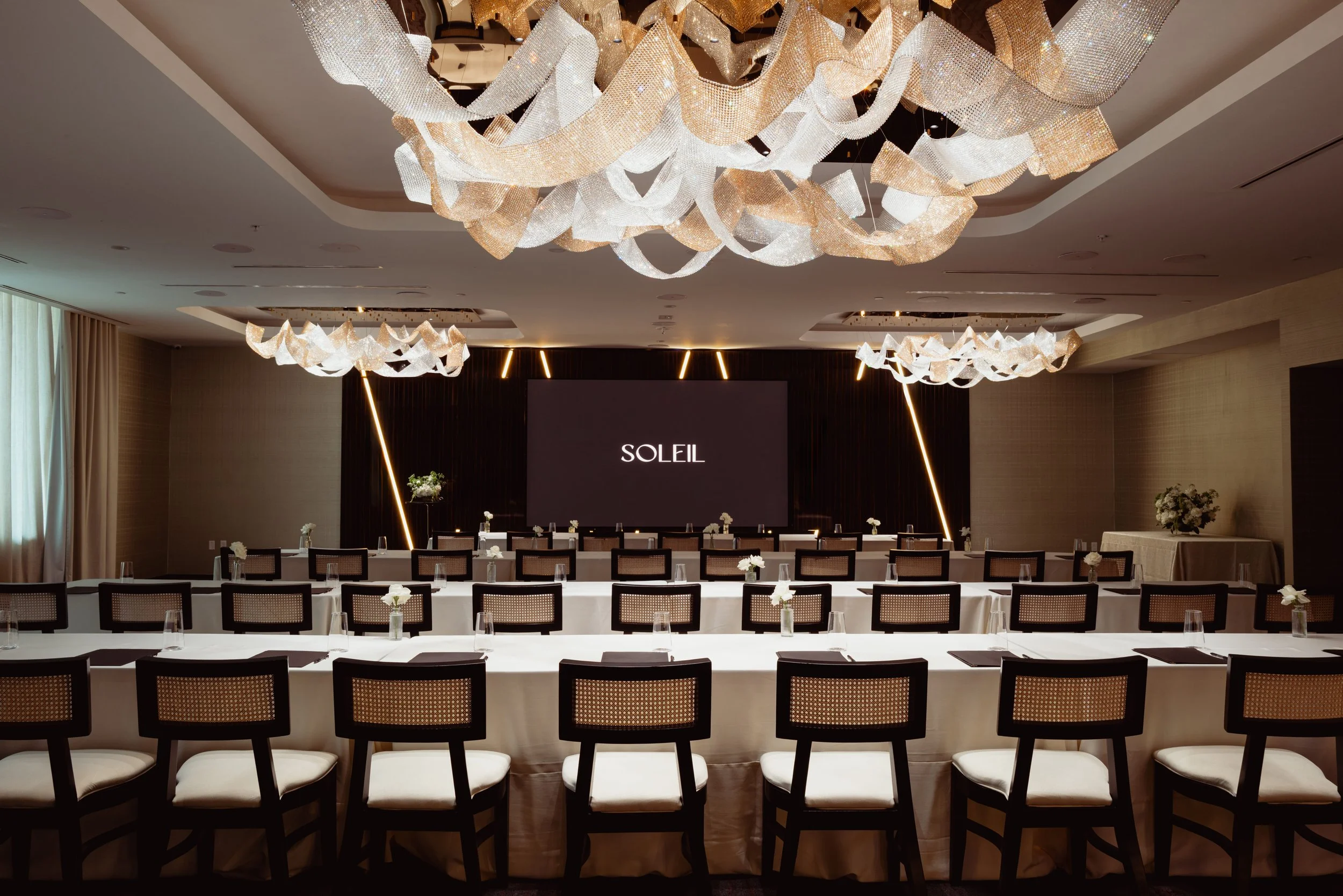 Three long rectangular tables facing LED screen