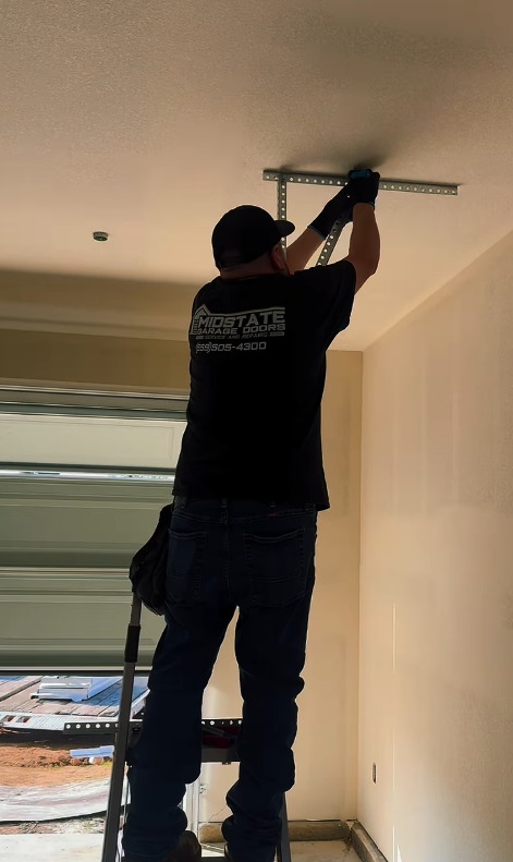 A person wearing a black shirt, jeans, and a cap is installing a metal support bracket on a ceiling.