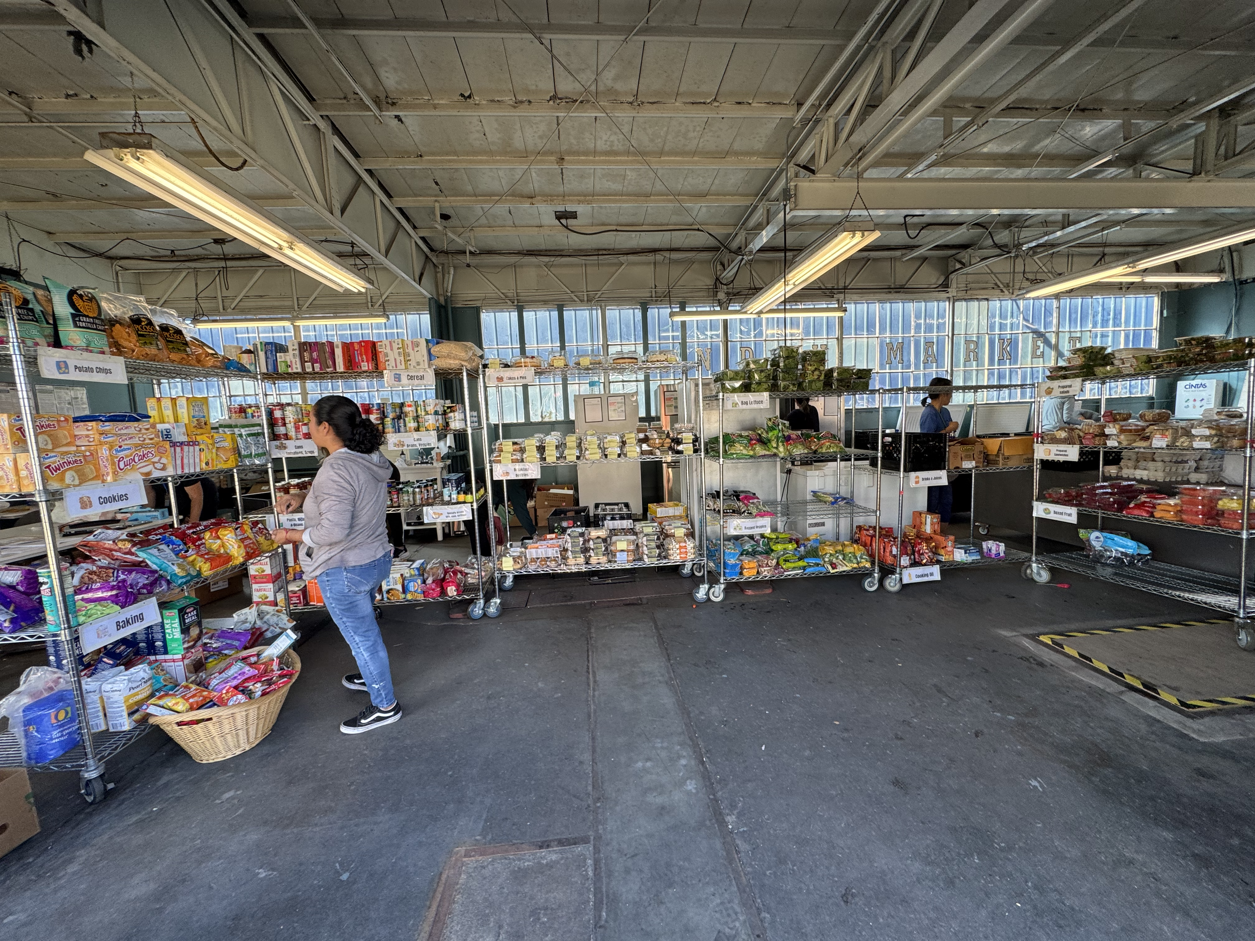 Interior view of a grocery store with shelves filled with various food products, shelves labeled 'Potato Chips,' 'Cookies,' 'Cereal,' and 'Baking.' Customers are shopping.