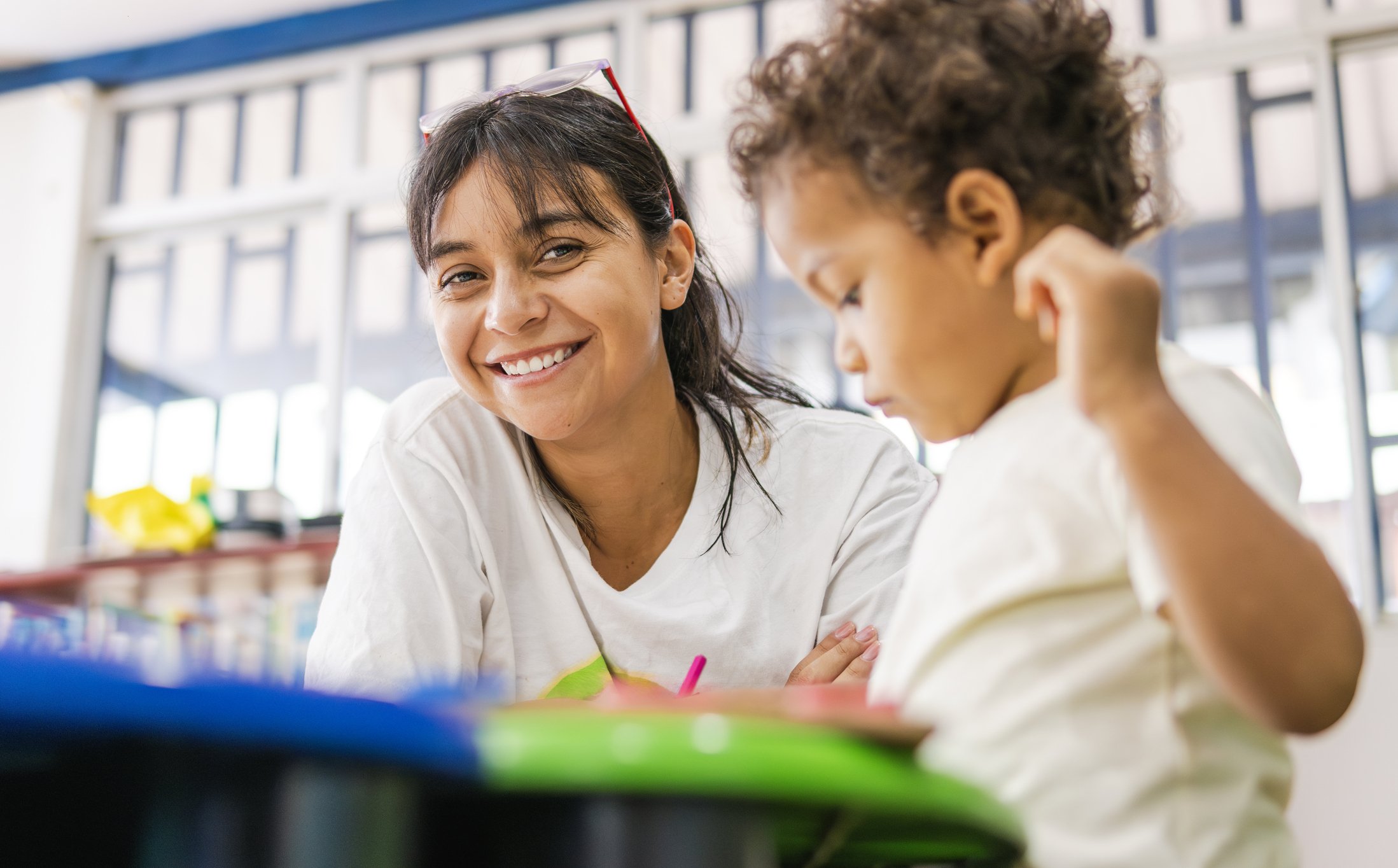 A woman smiling at a young boy in a classroom setting.