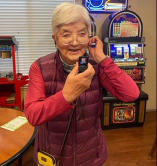 An elderly woman with short white hair talking on a landline phone while smiling, indoors with a cheery atmosphere.