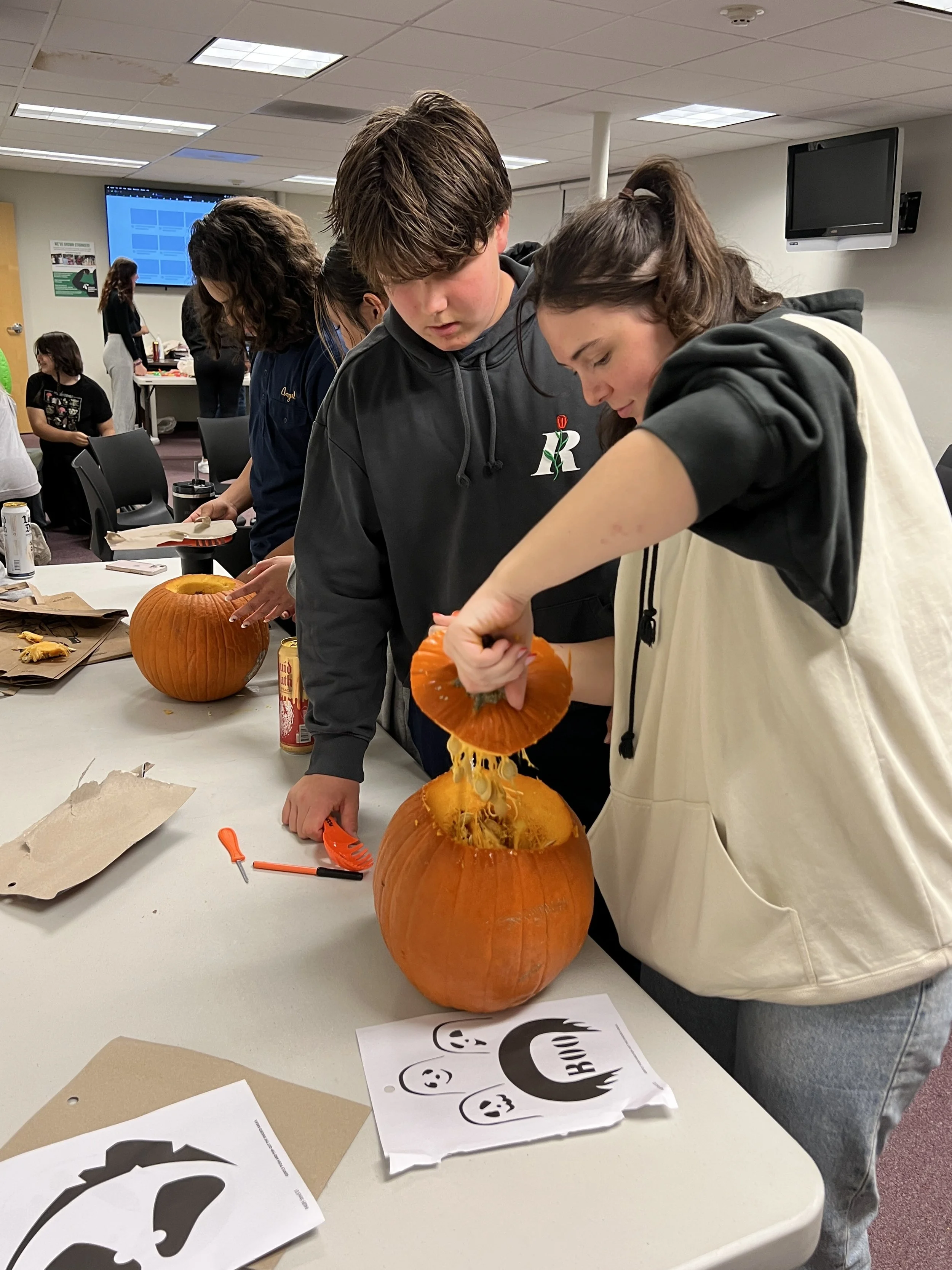 People carving pumpkins at a table during a Halloween event.