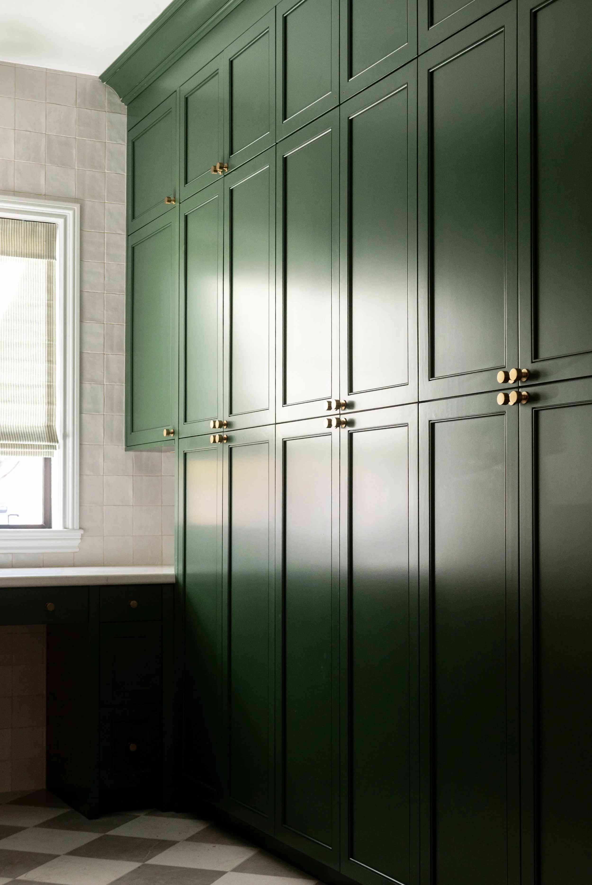 Green kitchen cabinets with gold knobs next to window with blinds.