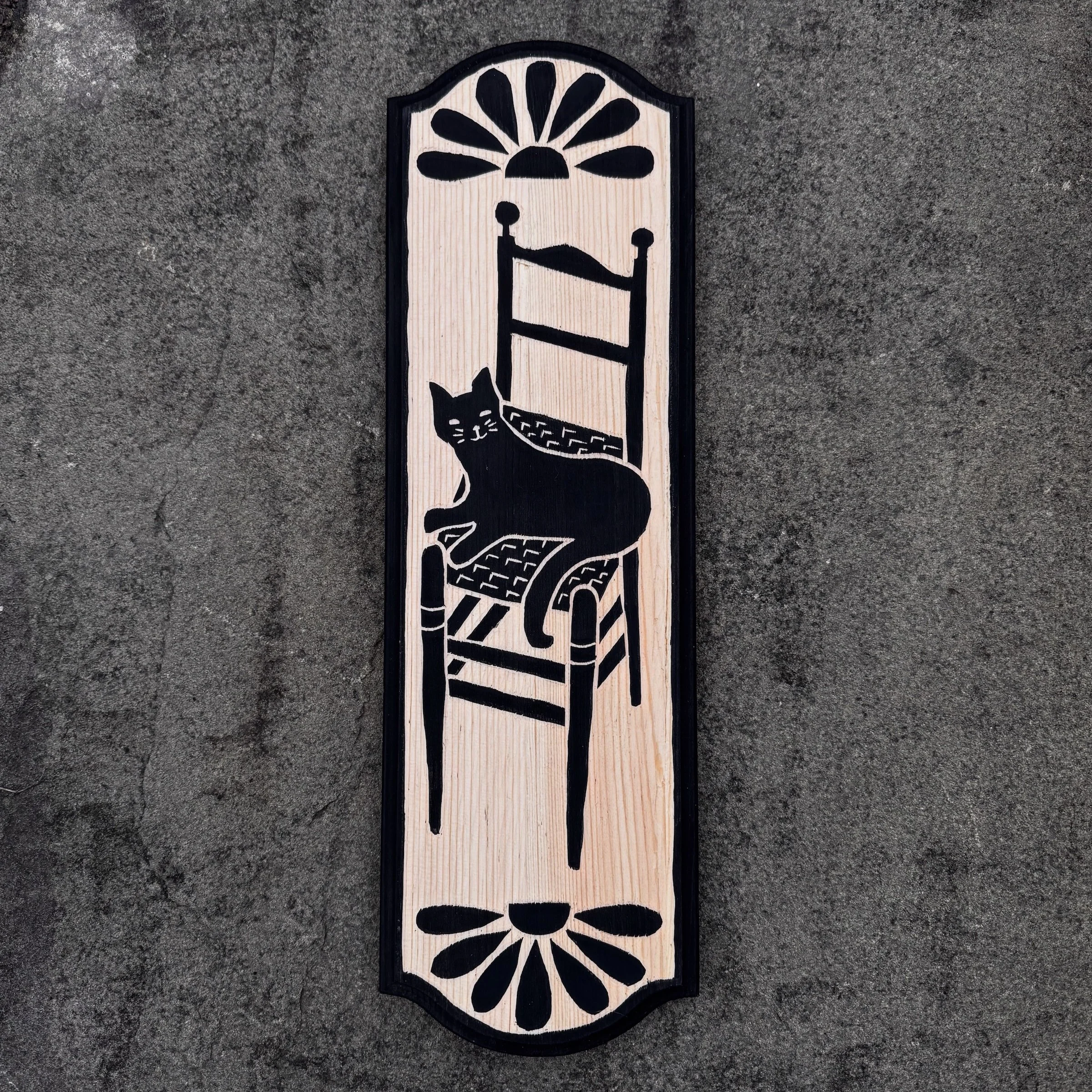 black and pine hand carved image of a black cat resting on a woven chair
