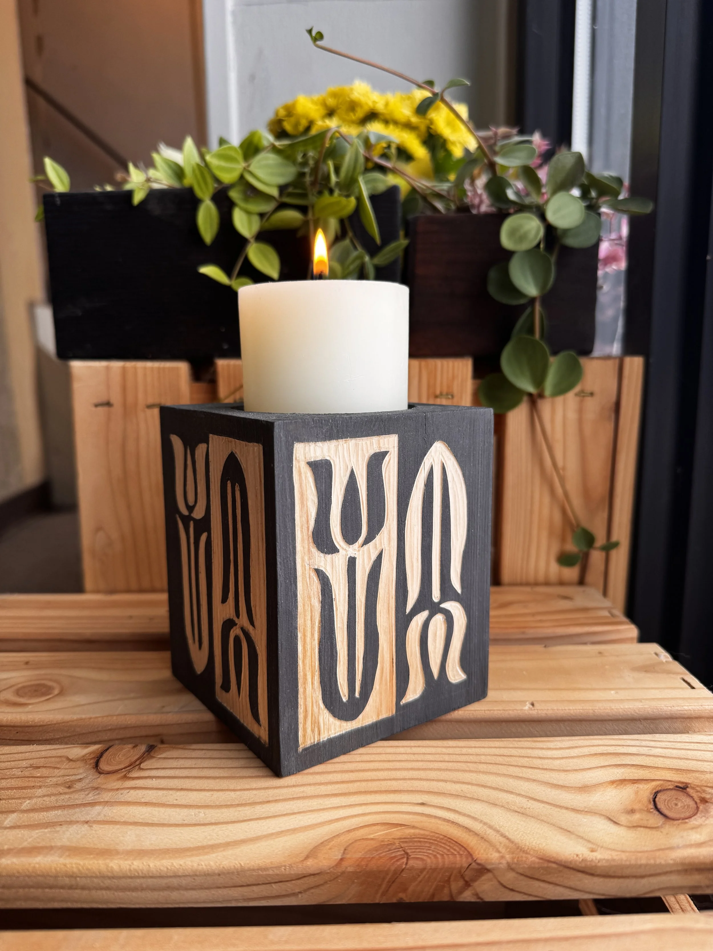 Black and pine, carved candle holder with a white pillar candle lit in center