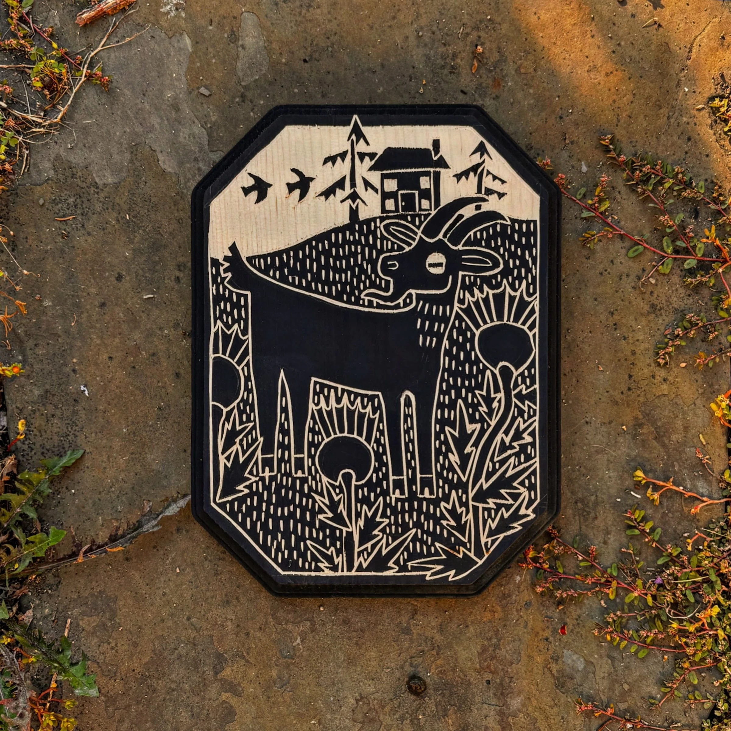 a lone goat stands in the middle of a field surrounded by thistle with a small home behind it, hand carved pine with black paint