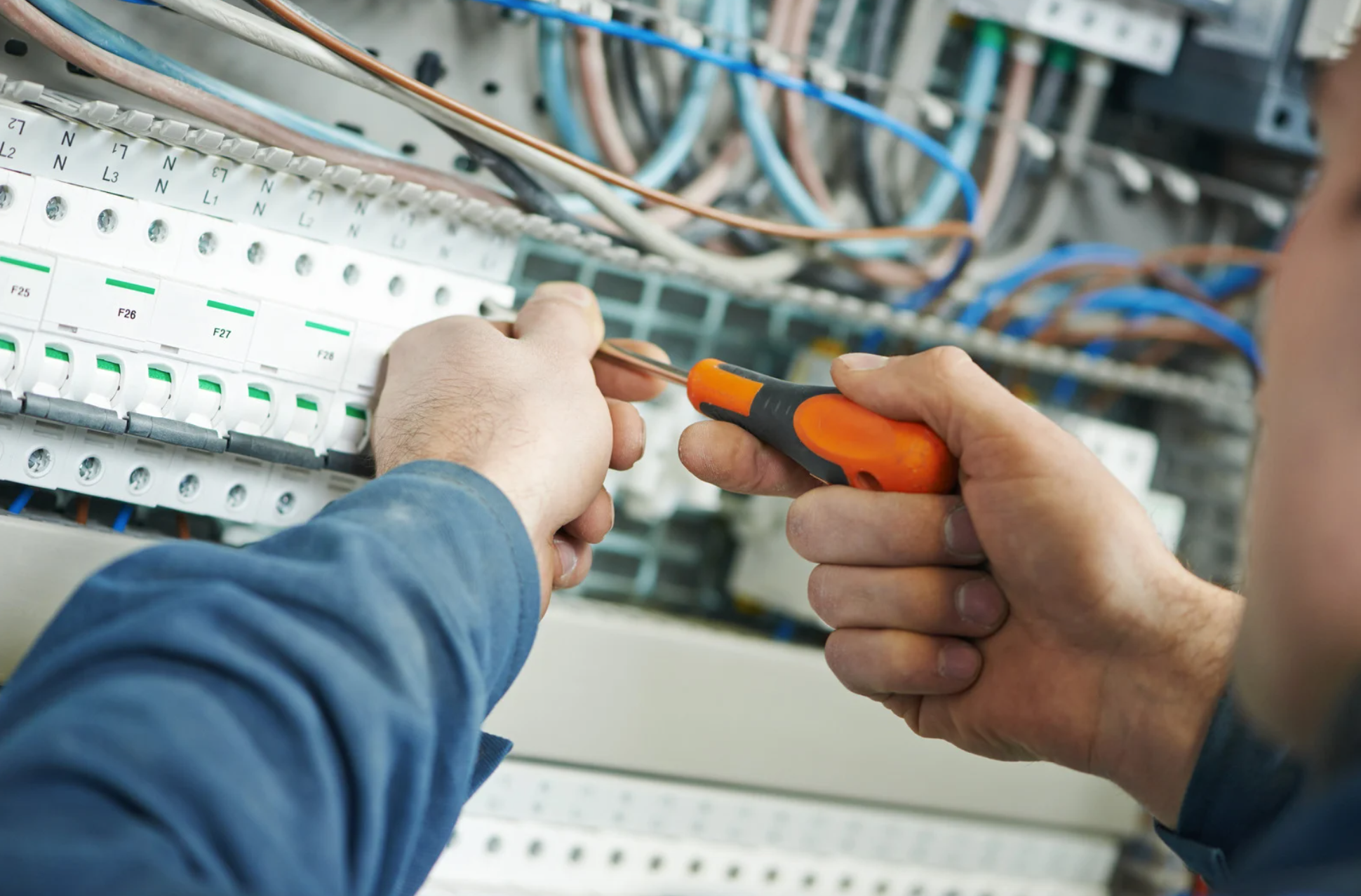 Electrician working on consumer unit with lots of blue and brown wires in background.