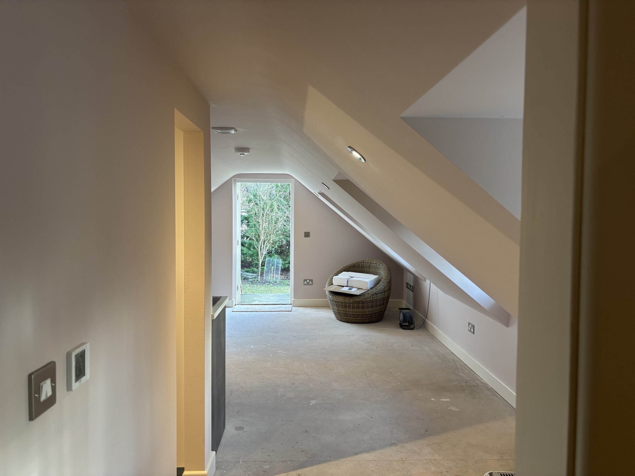 Loft conversion with rattan chair in corner. lights fitted in ceiling and heating controls on the wall