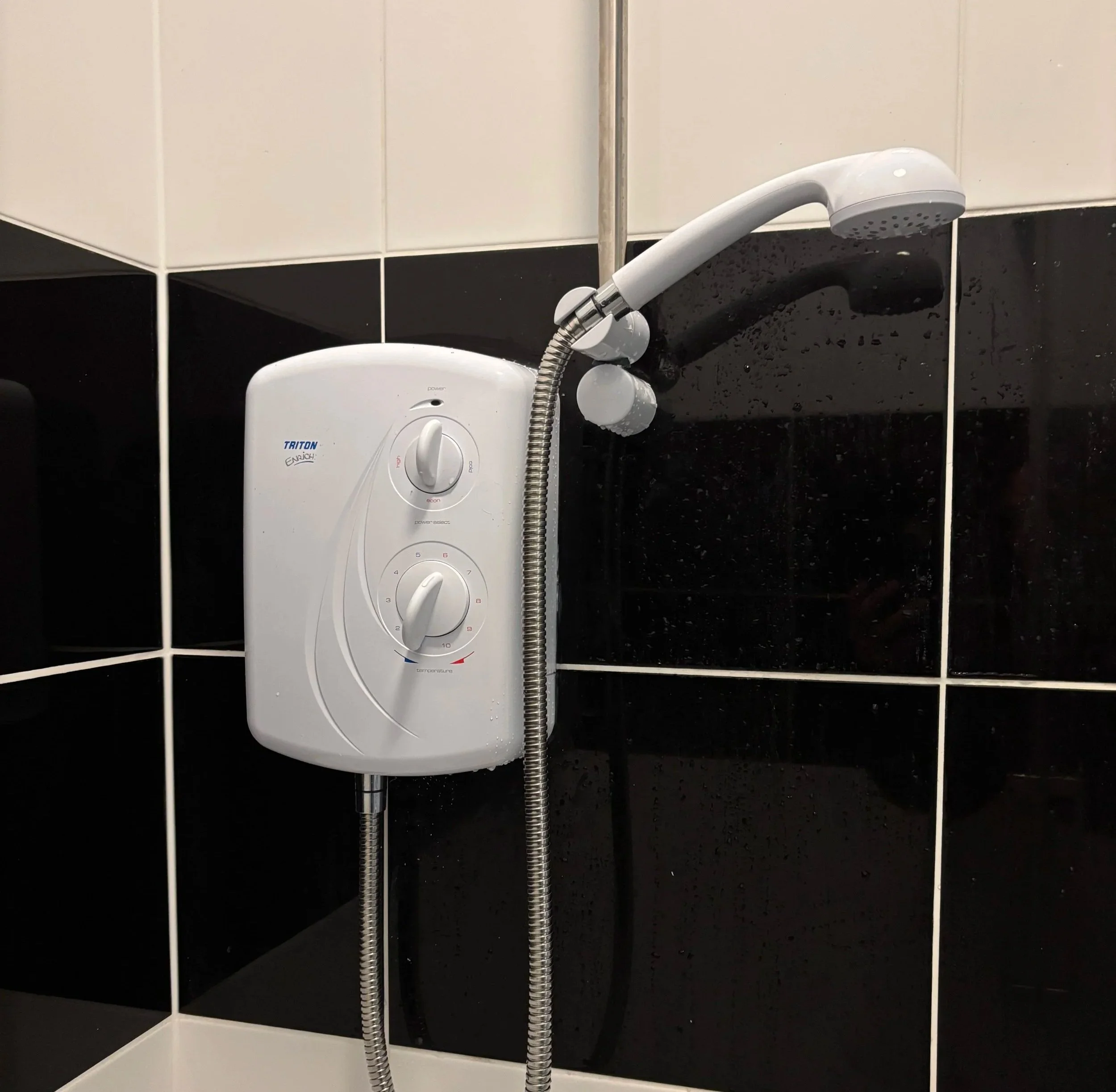Electric shower on wall decorated with black and white tiles