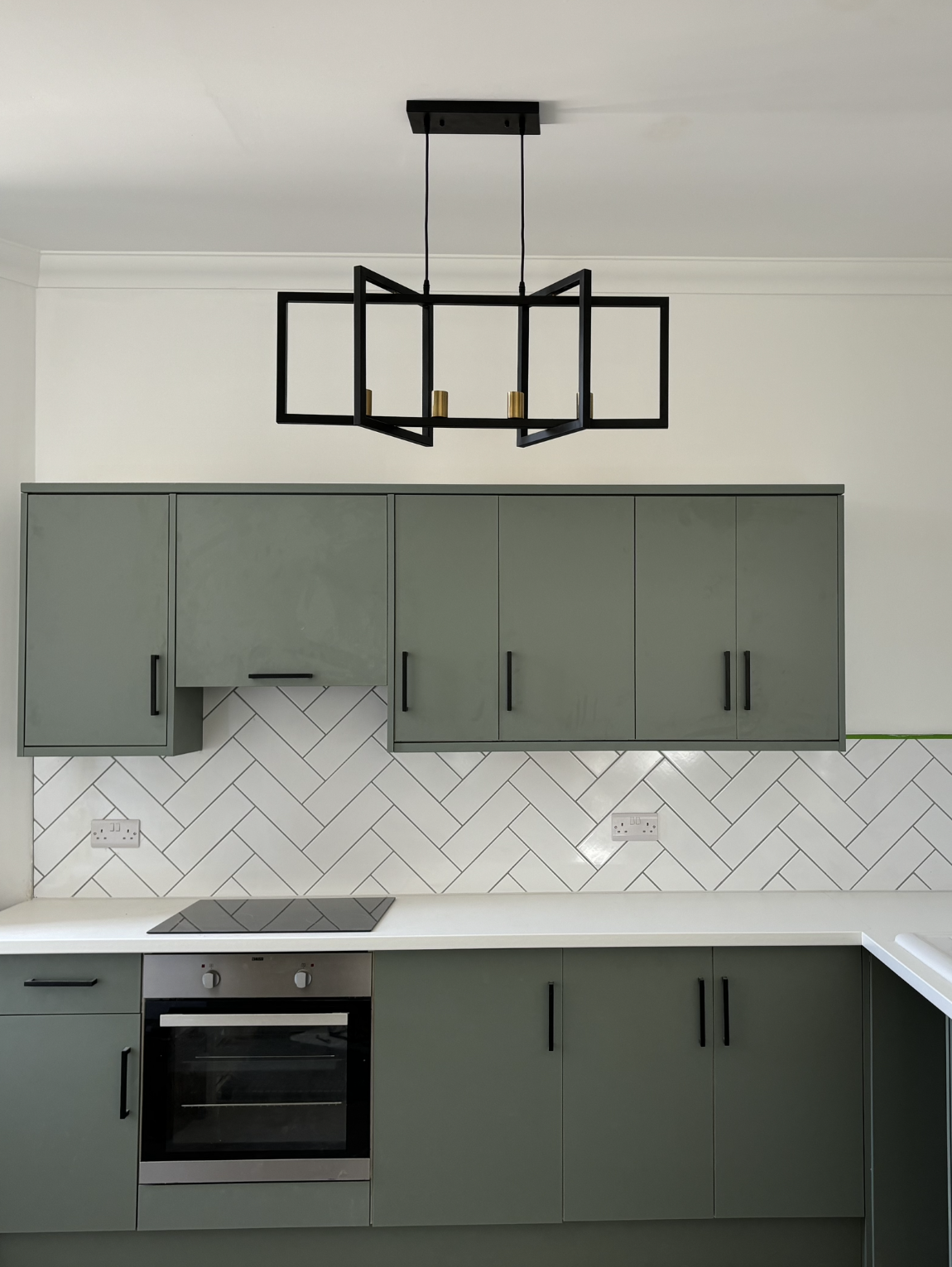 Modern kitchen with green cupboards and white worktops. Black and silver oven with black light fitting