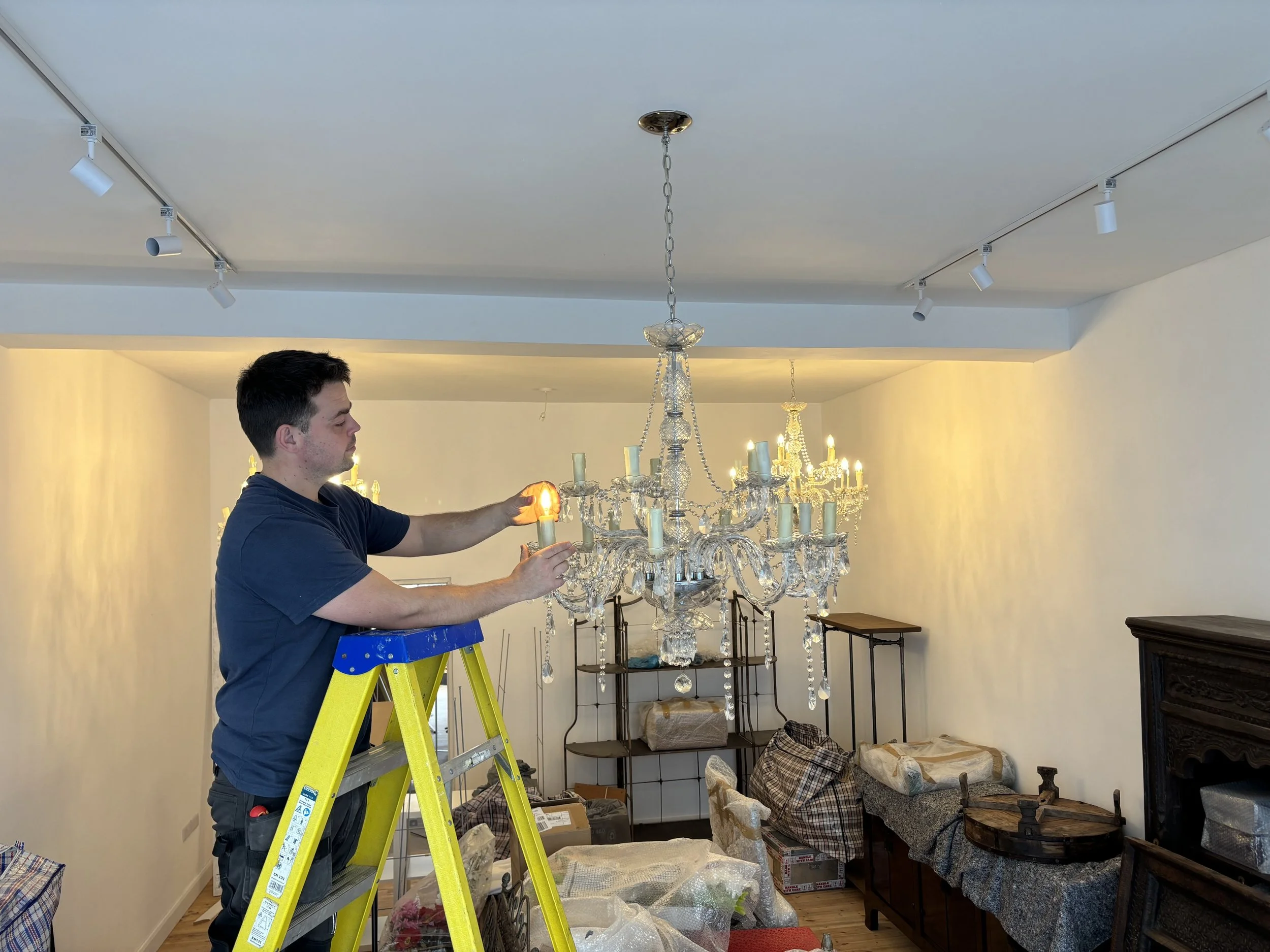 man on yellow and blue ladder putting bulb into chandelier