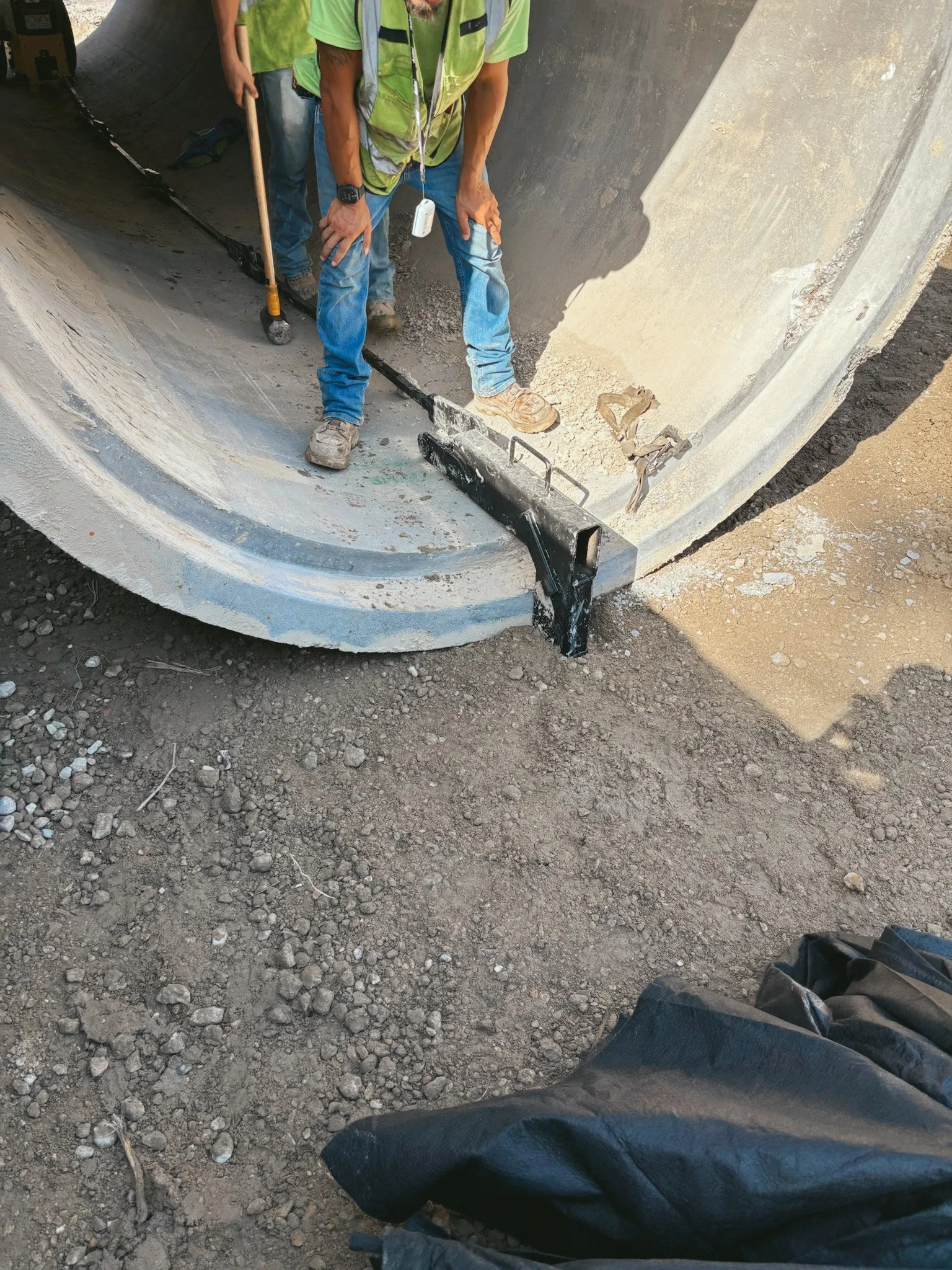 Construction workers standing inside a large concrete pipe at an outdoor construction site.