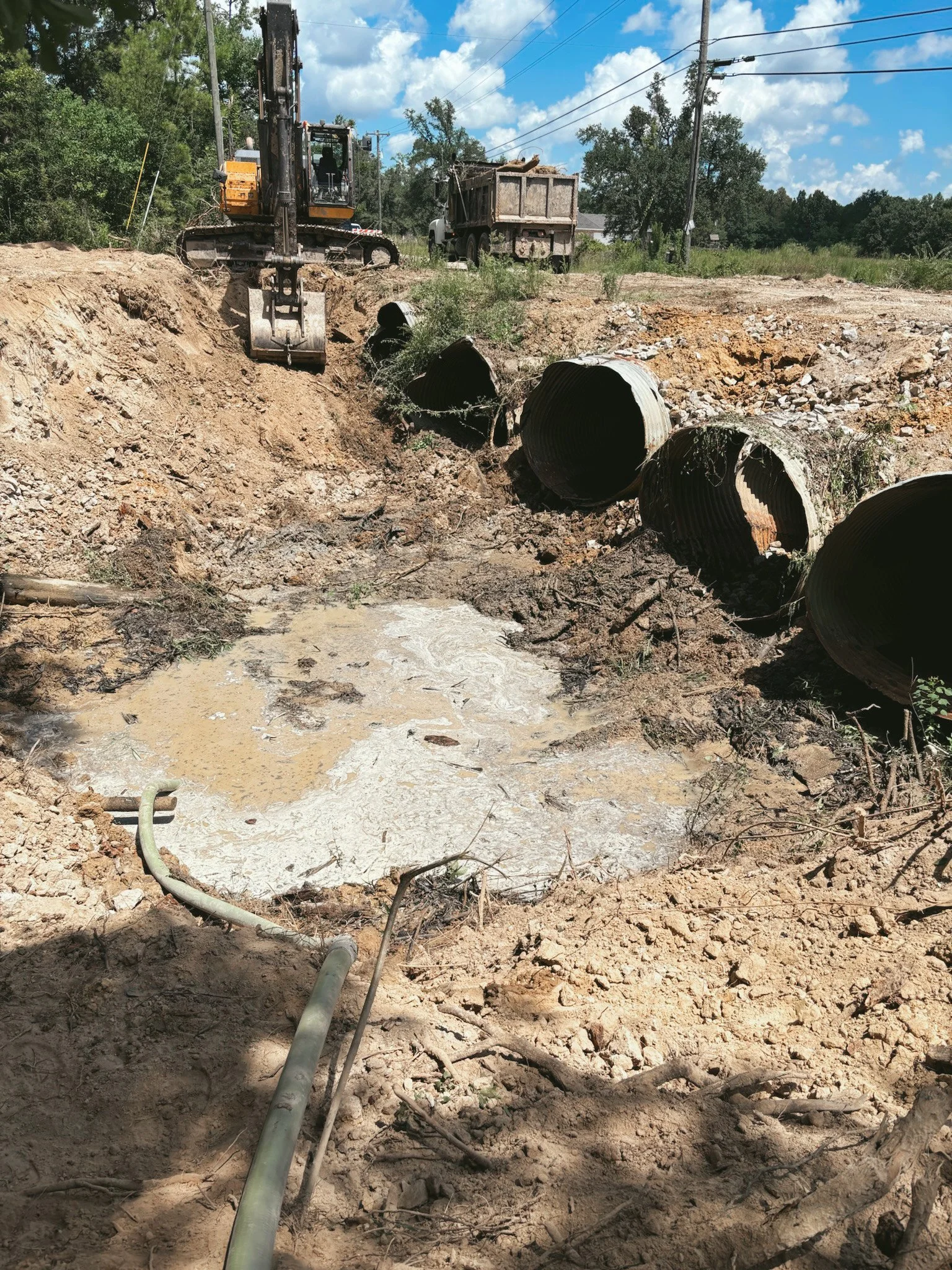 Construction site with large pipes, excavator, truck, and muddy puddle.