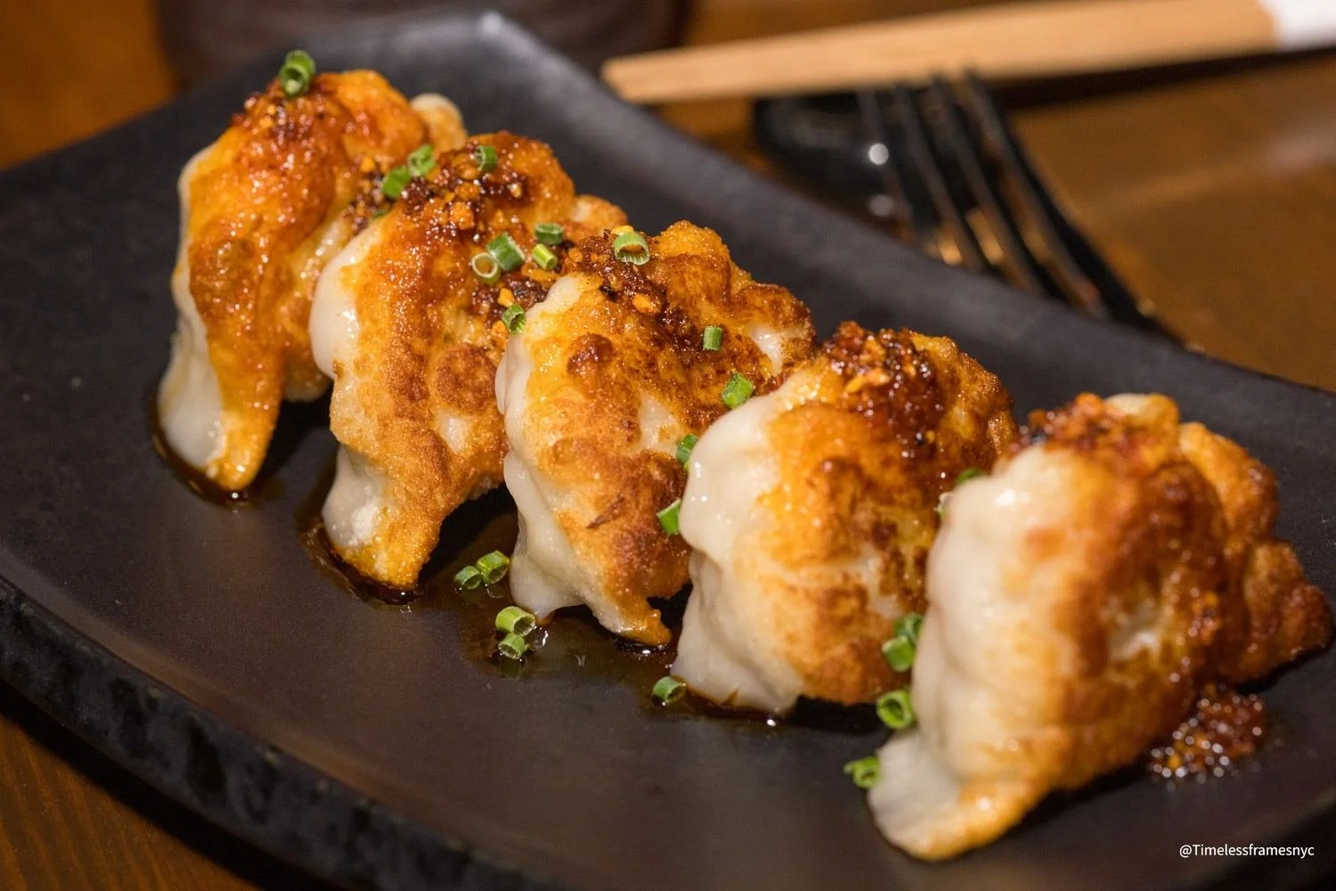 Row of pan-fried dumplings with chili crisp and scallions on a slate plate