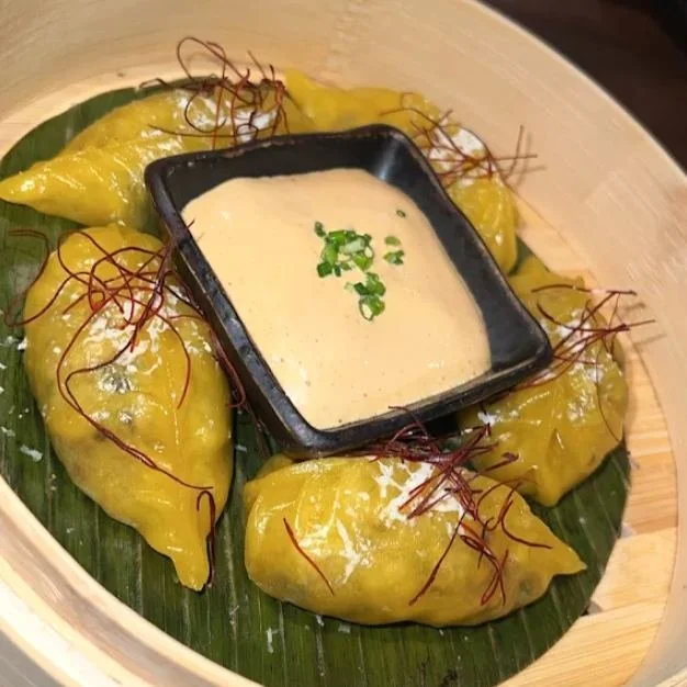 Yellow dumplings on a banana leaf in a bamboo steamer with a creamy dipping sauce