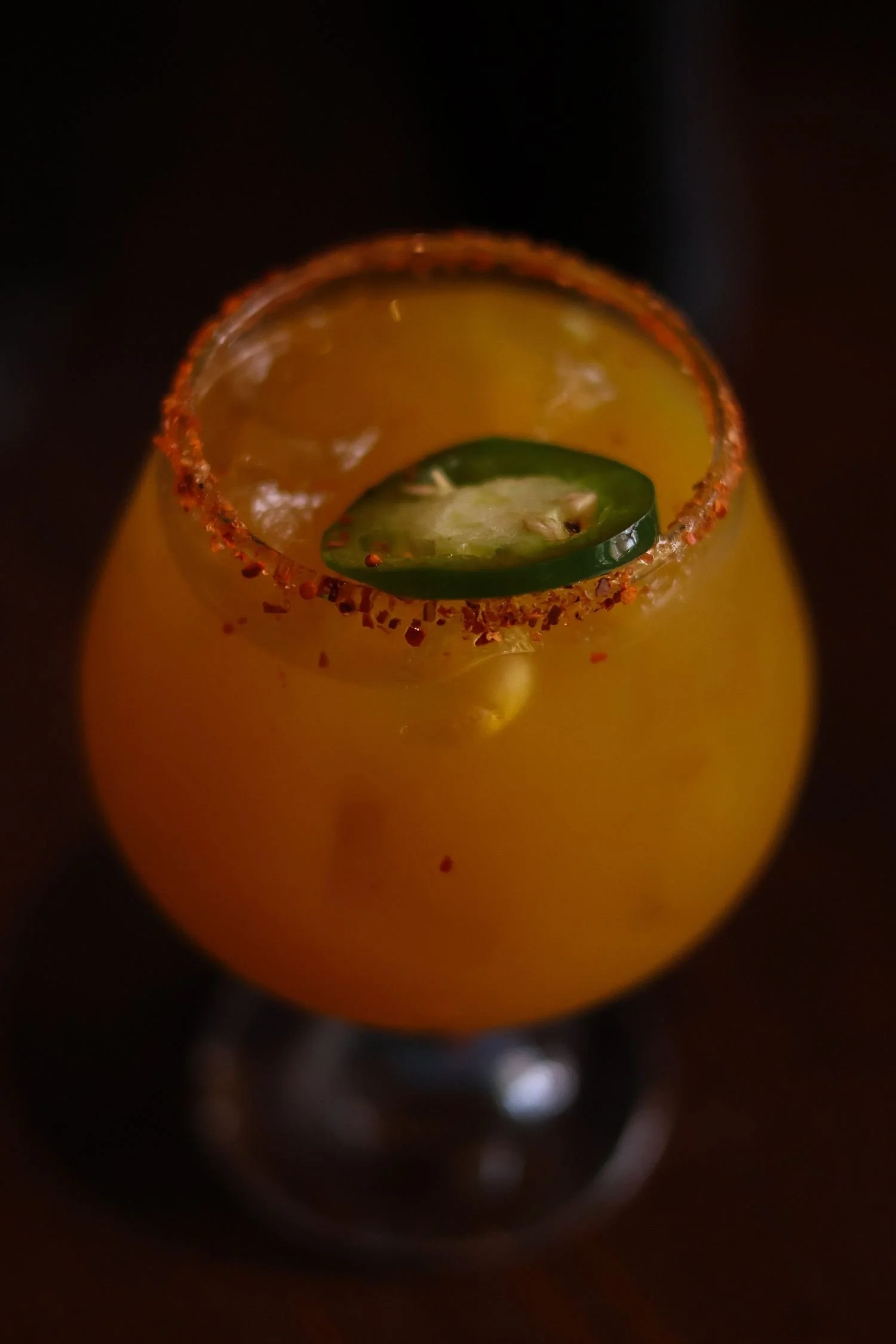 Orange cocktail with a chili-salt rim and a jalapeño slice