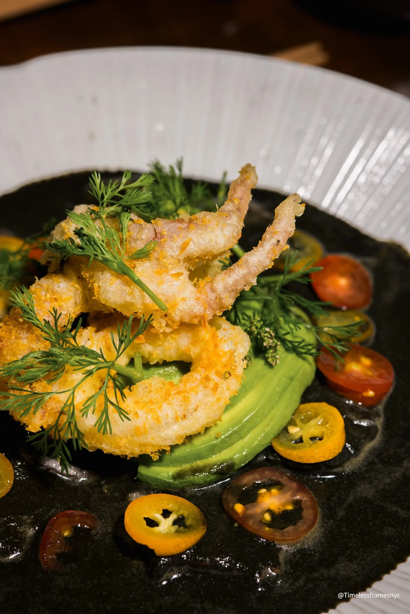 Fried shrimp on a bed of sliced cucumber, garnished with fresh herbs and cherry tomato slices on a black plate.