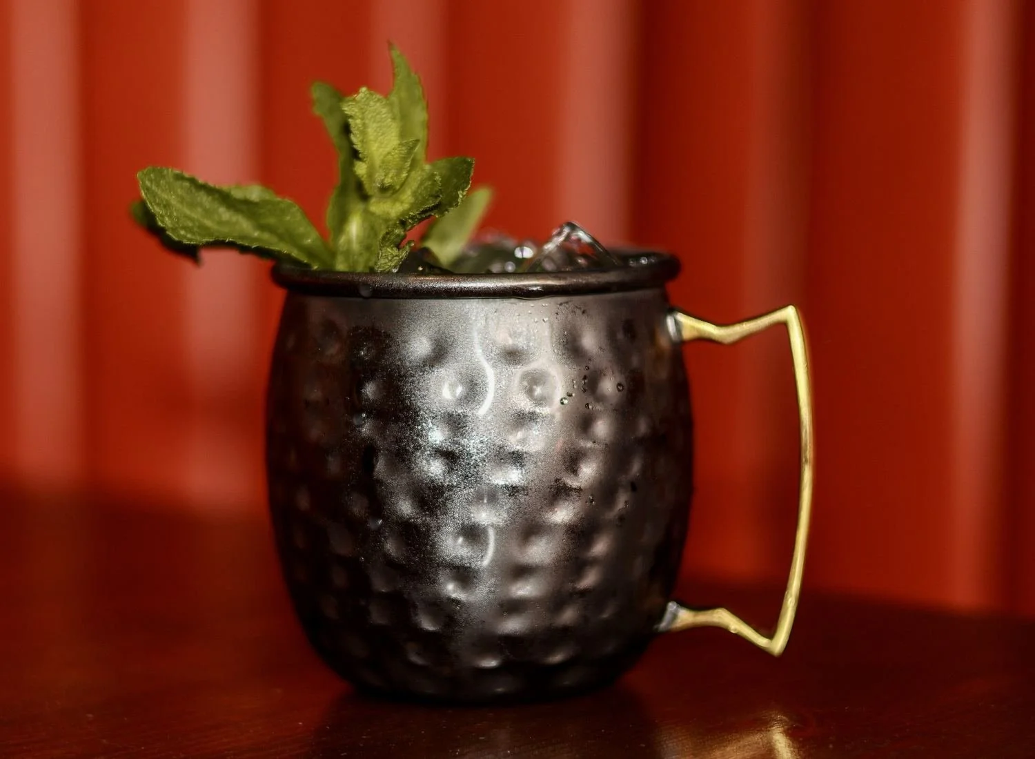 Cocktail with crushed ice and fresh mint in a hammered dark metal mug with a gold handle