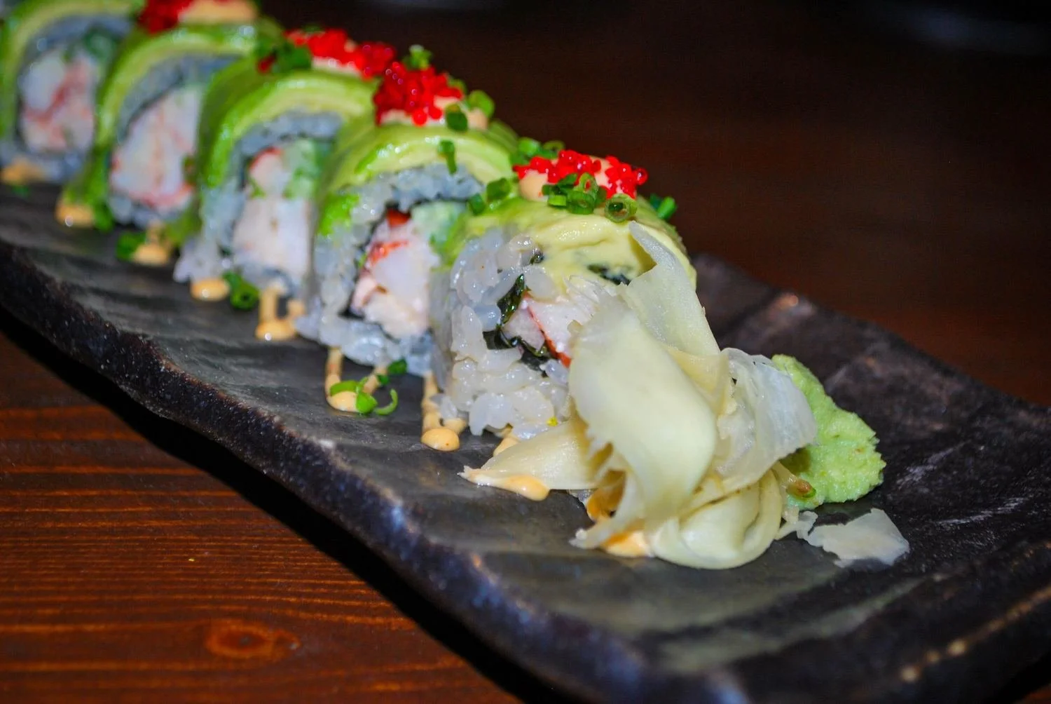 Avocado-topped sushi roll with red tobiko, pickled ginger and wasabi
