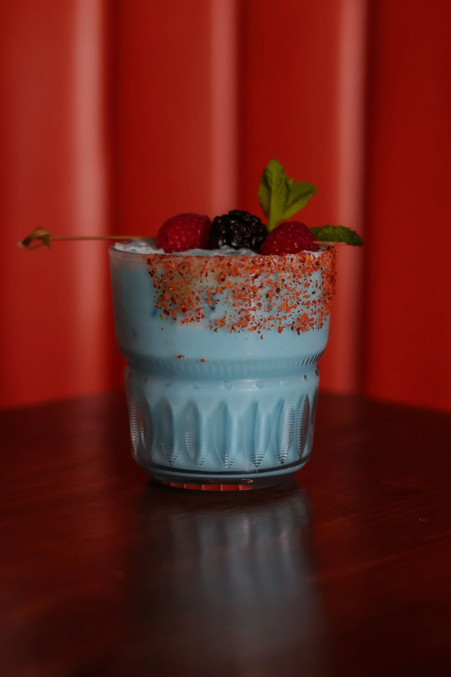 Light blue cocktail with a chili-salt rim, topped with berries and mint