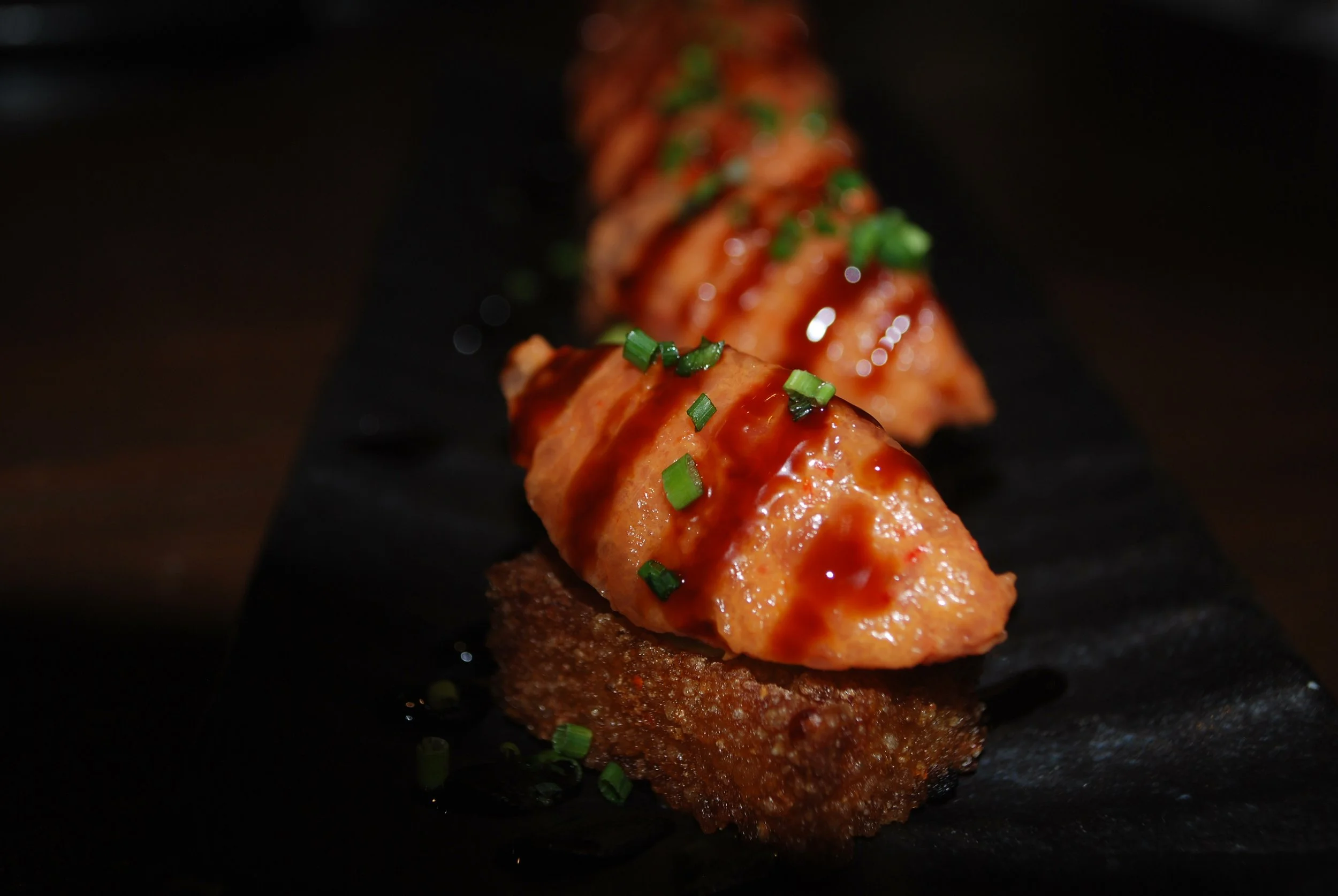 Chinaloa Sushi rolls with salmon, topped with green onions and sauce, placed on a black serving board.