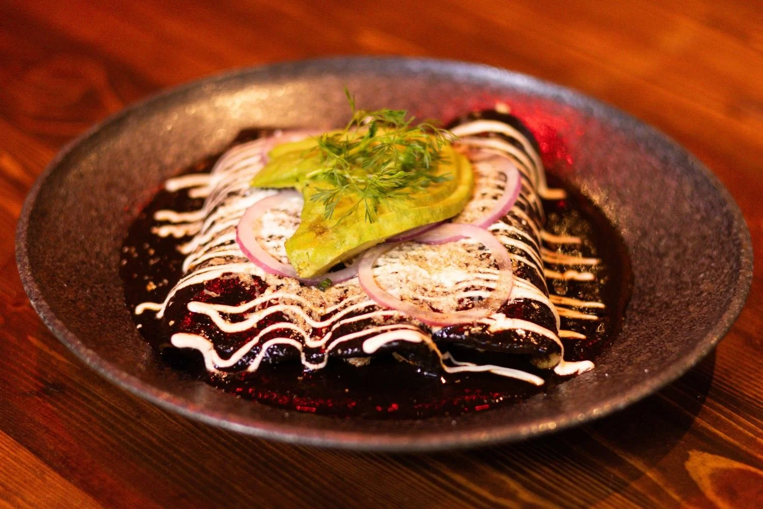 Enchiladas topped with cream, avocado and red onion