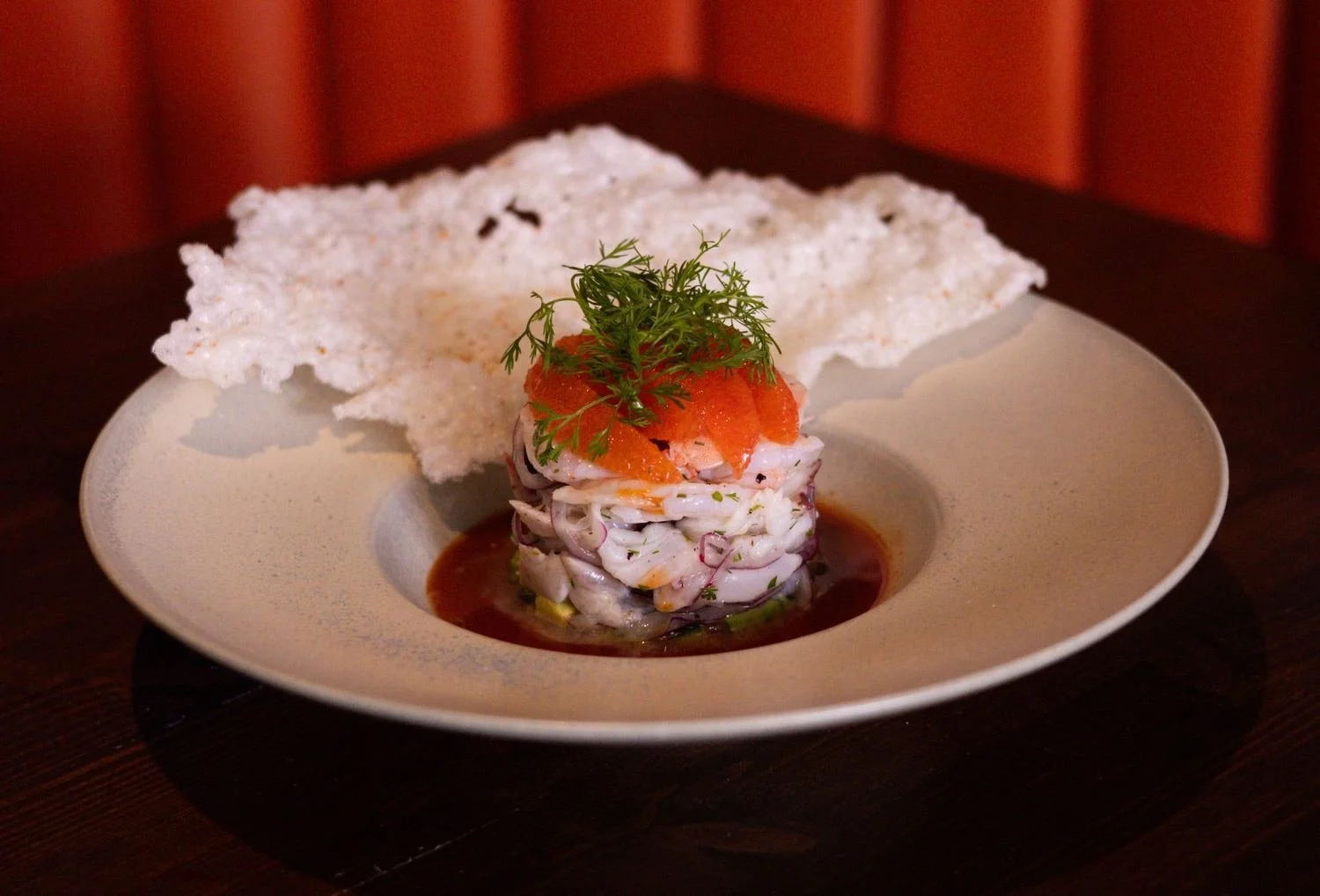 Stacked aguachile topped with tomato and dill, served with a crisp rice cracker