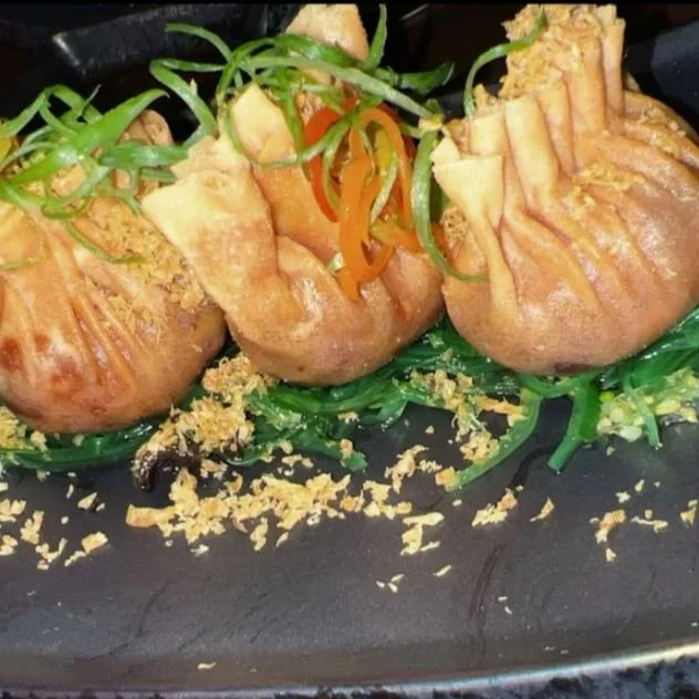 Crispy dumpling purses on seaweed salad, topped with fried garlic and shredded vegetables