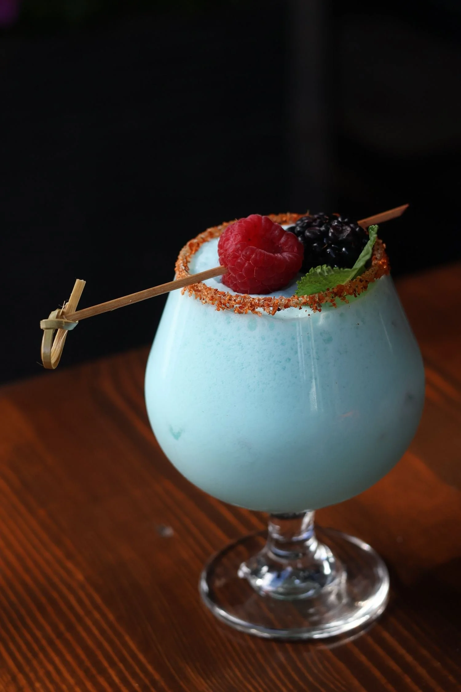 Light blue cocktail with a chili-salt rim and berries on a bamboo pick
